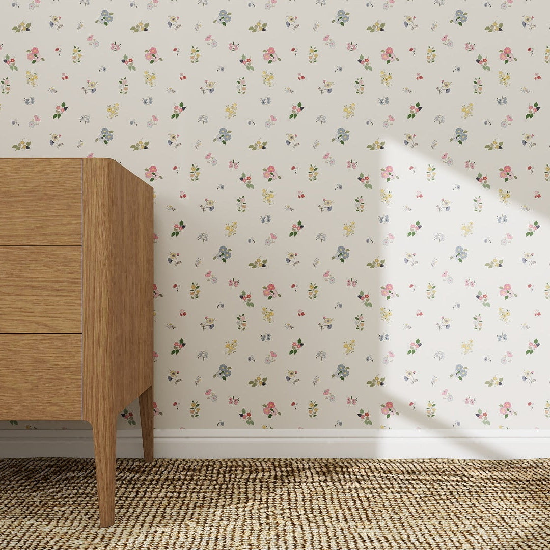 A mid-century modern wooden dresser stands on a woven rug near a wall featuring the Powdered Petals Wallpaper sample. Sunlight casts a shadow, creating a bright and airy atmosphere.