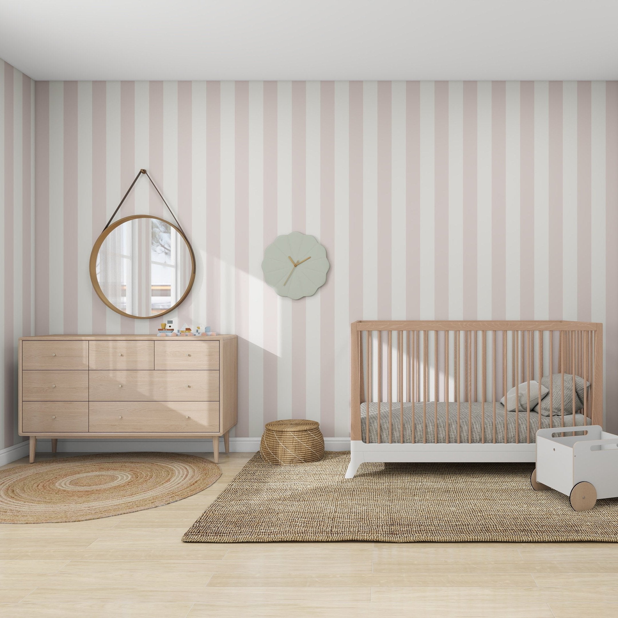 A cozy kids space with munks and mes Circus Stripe Wallpaper Blush Rose features a wooden crib, a dresser with a round mirror above, a round woven rug, small basket, decorative wall clock, white toy cart, all on an expansive beige rug.