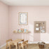 A childs room includes a small wooden table and chairs on a woven rug, surrounded by Cherry Red Sprinkle Wallpaper samples. Decor adorns the walls, with a framed poster, colorful shelves for toys, and a pegboard. A closed wardrobe sits on the right with an adjacent mirror.