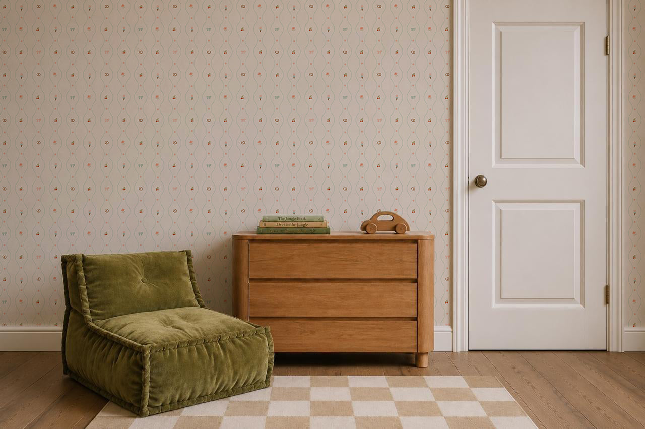 A modern room with a green lounge chair, a wooden dresser topped with stacked books and a toy, a white door, and a checkered rug on wooden floors. The Little Patisserie Stripe Wallpaper features subtle hand-drawn stripes, adding an artistic touch to the serene space.
