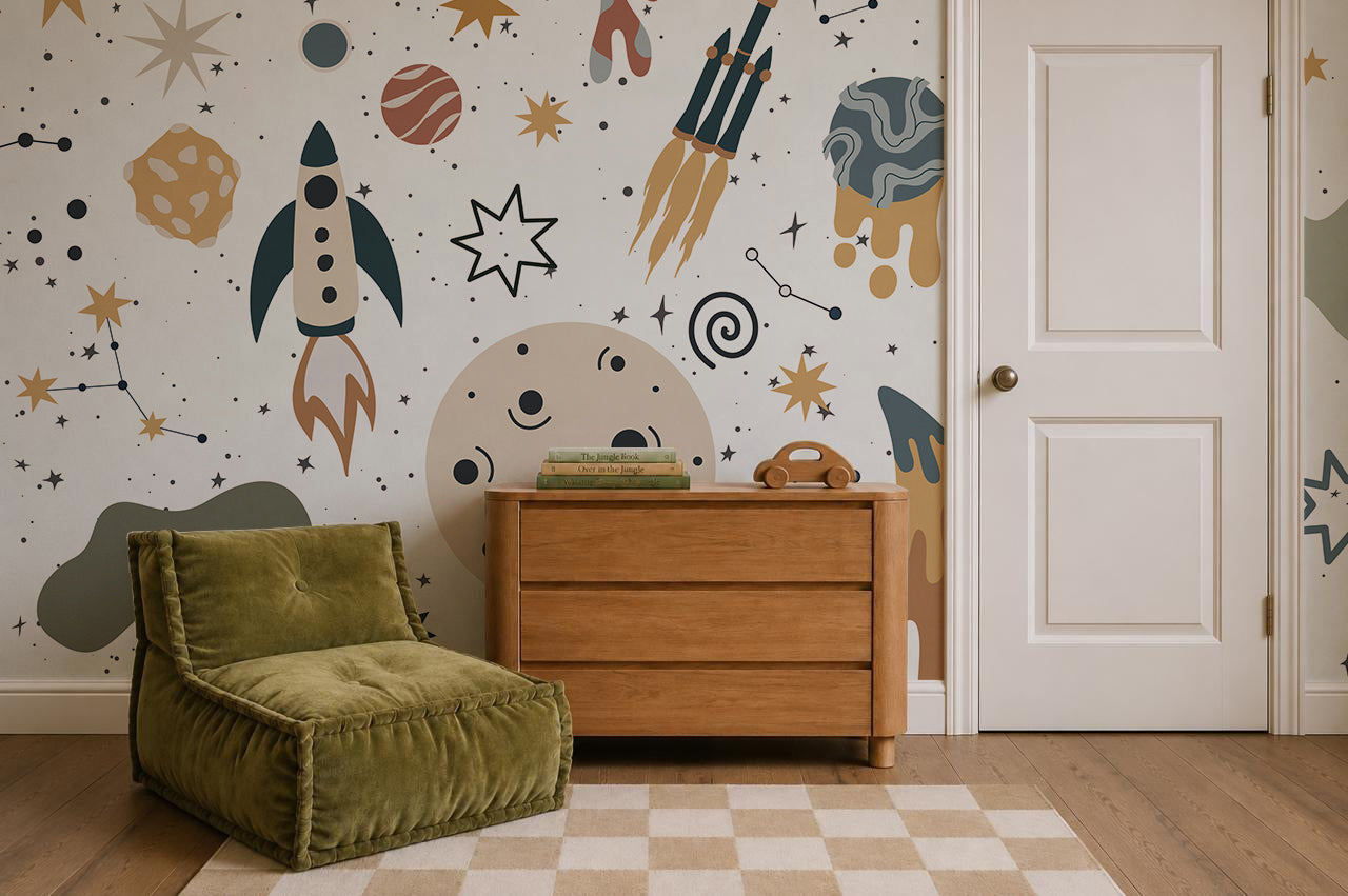 A cozy room with a green chair, wooden dresser, books, and a toy phone. The feature wall displays the vibrant To The Moon Mural, filled with rockets, planets, stars, and abstract shapes for an inspiring space-themed atmosphere.