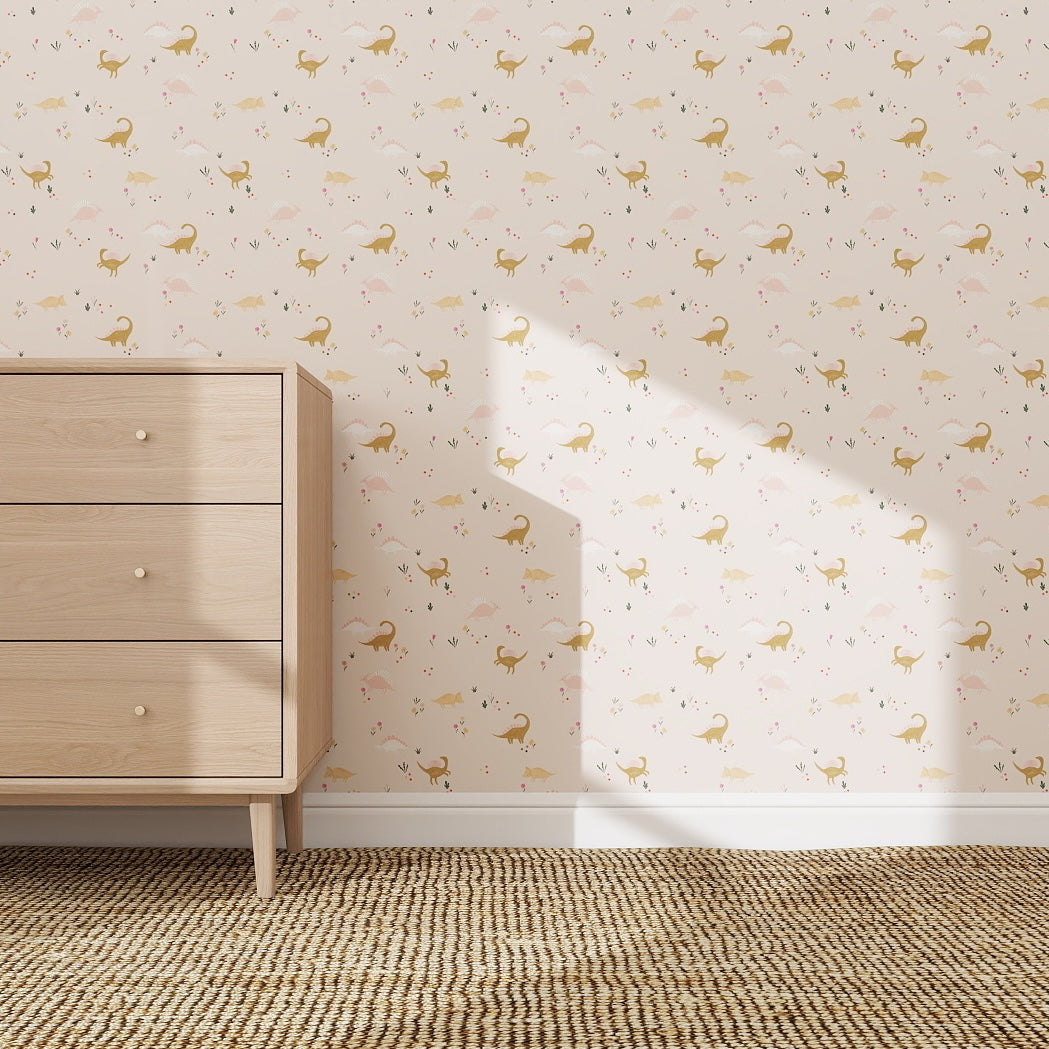 A light wood dresser stands on a beige textured rug. The wall features Dixie Dinosaur Repeat Pattern Wallpaper with small dinosaurs and plants in soft pastels, while sunlight casts a shadow across the scene.