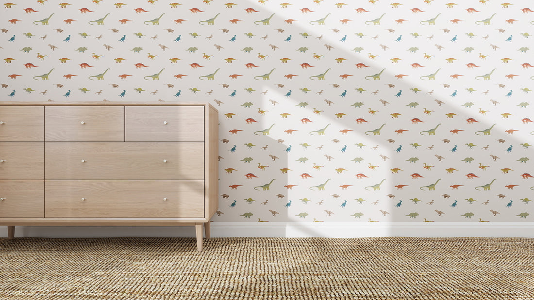 A light wood dresser stands on a woven rug before a white wall featuring the Dino Discovery Repeat Wallpaper Pattern, ideal for young explorers. Sunlight casts diagonal shadows over this playful scene.