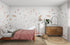 The bedroom showcases the Fish Tank Wallpaper Mural by munks and me, depicting sea life with fish, turtles, and jellyfish. On the left sits a pink-dressed wooden bed; on the right, a rustic dresser with a mirror and plant. A lamp stands nearby on a woven rug enhancing the rooms aquatic vibe.