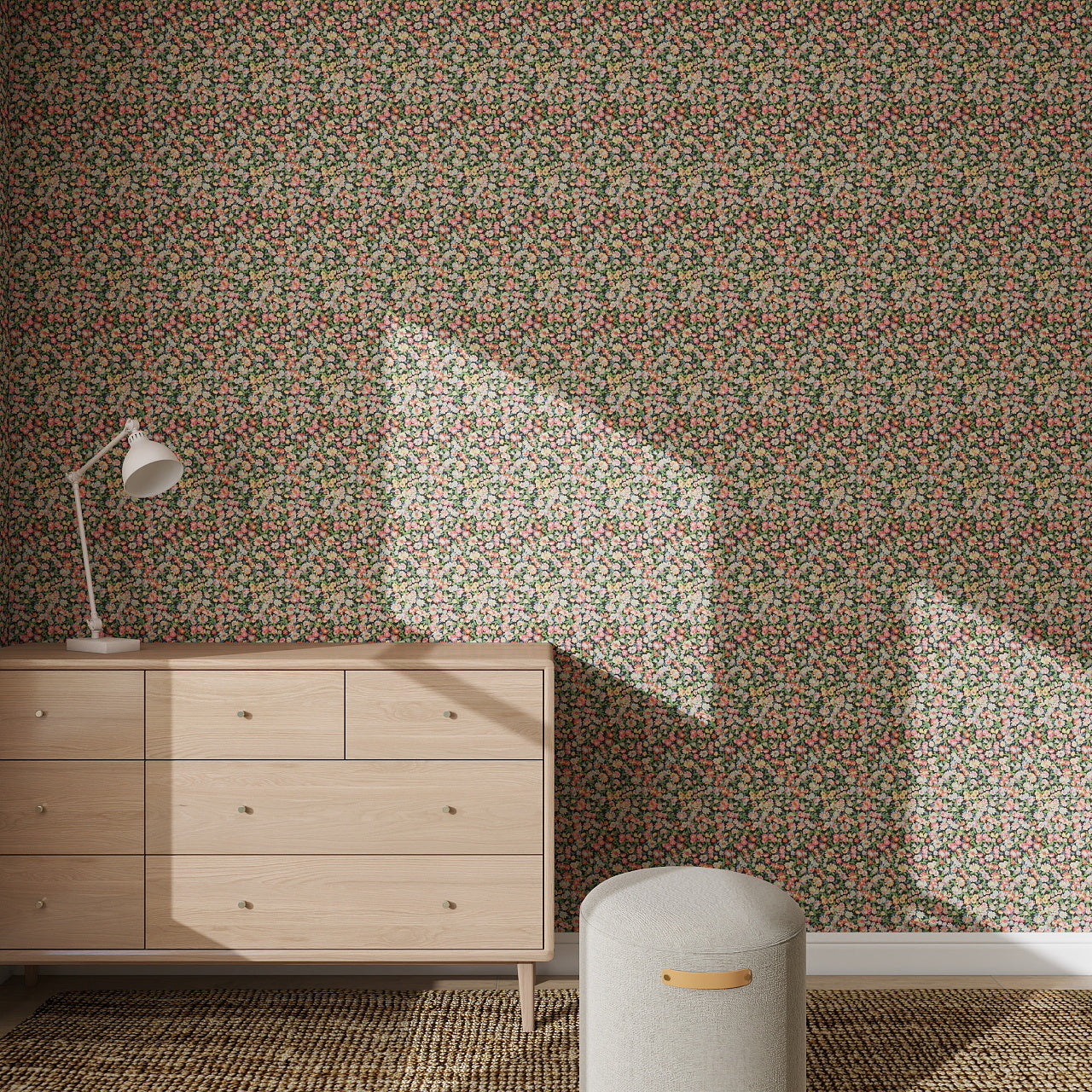 A wooden dresser with a white desk lamp stands against a wall covered in the Midnight Meadow Florals Wallpaper. Sunlight casts window-shaped shadows across the room, while a small round ottoman sits on a woven rug.