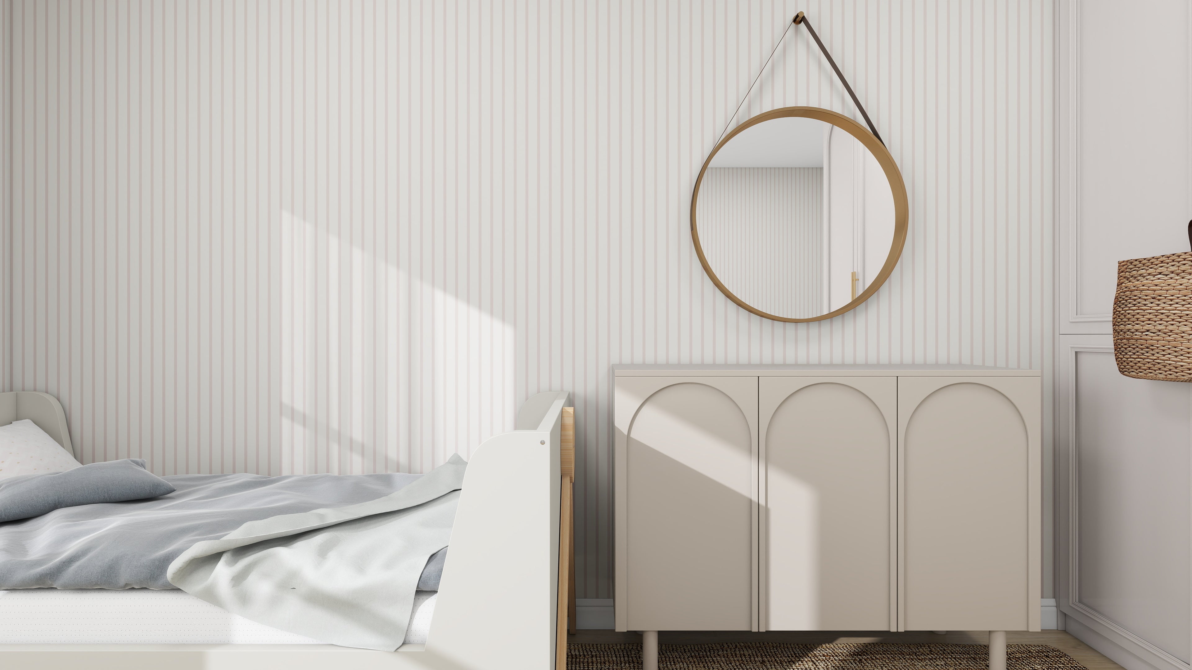 A minimalist bedroom features a light wooden bed draped with blue and white bedding. Adjacent is a beige cabinet with arch patterns, and above it hangs a round mirror with a leather strap on munks and mes Pinstripe Wallpaper Blush Rose; sunlight filters in, casting shadows through the window.