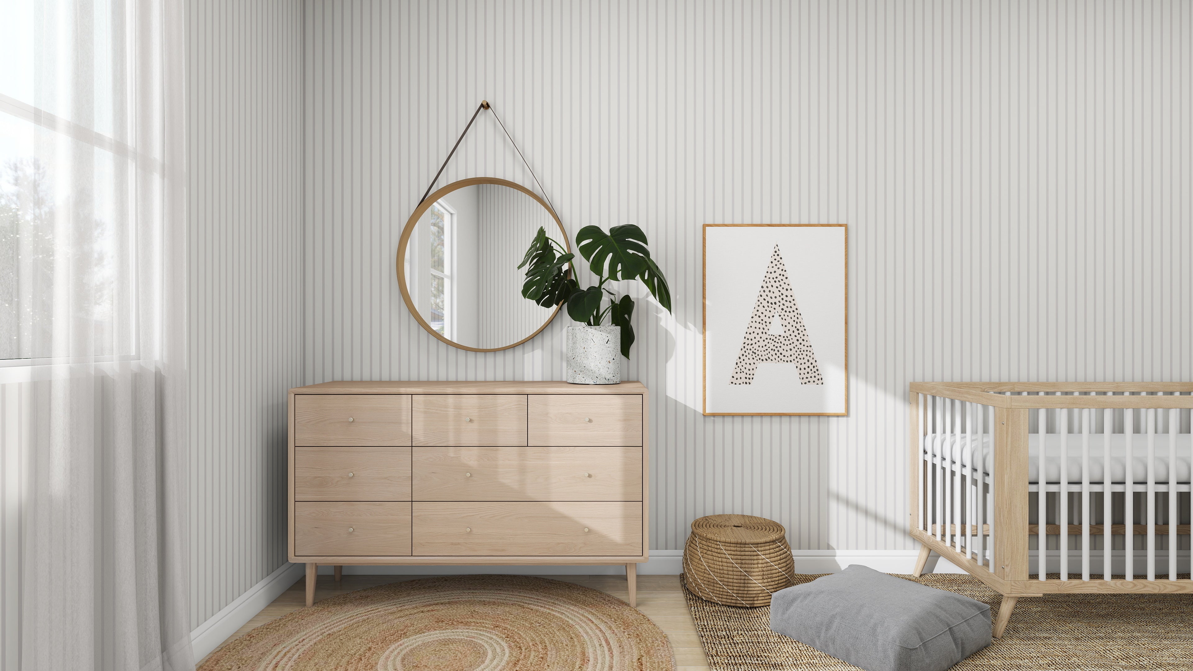 A minimalist nursery includes light wood furniture—a dresser, crib, and round mirror. Accents like a framed A and plant sit on the dresser. A woven rug, basket, and gray cushion rest on Pinstripe Wallpaper Soft Beige by munks and me.