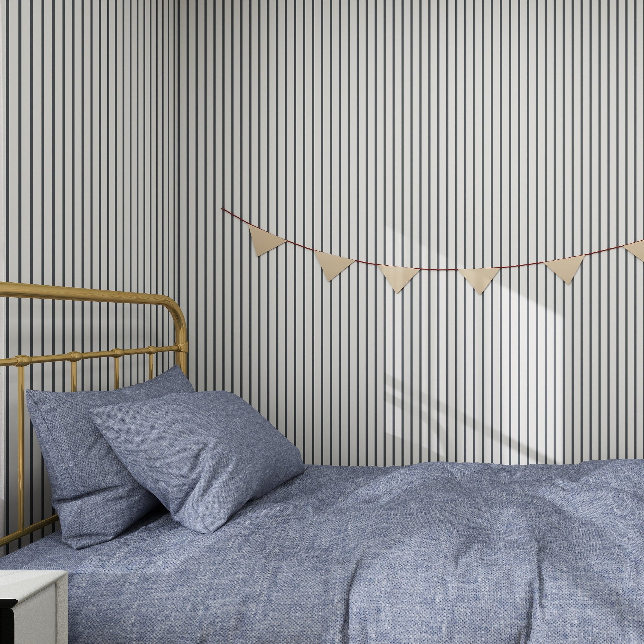 A cozy bedroom showcases a neatly made bed with blue bedding and a vintage brass headboard. The walls are adorned with munks and mes Pinstripe Wallpaper Denim, while a triangular pennant banner adds charm. Soft blush rose accents bring warmth to this inviting space.