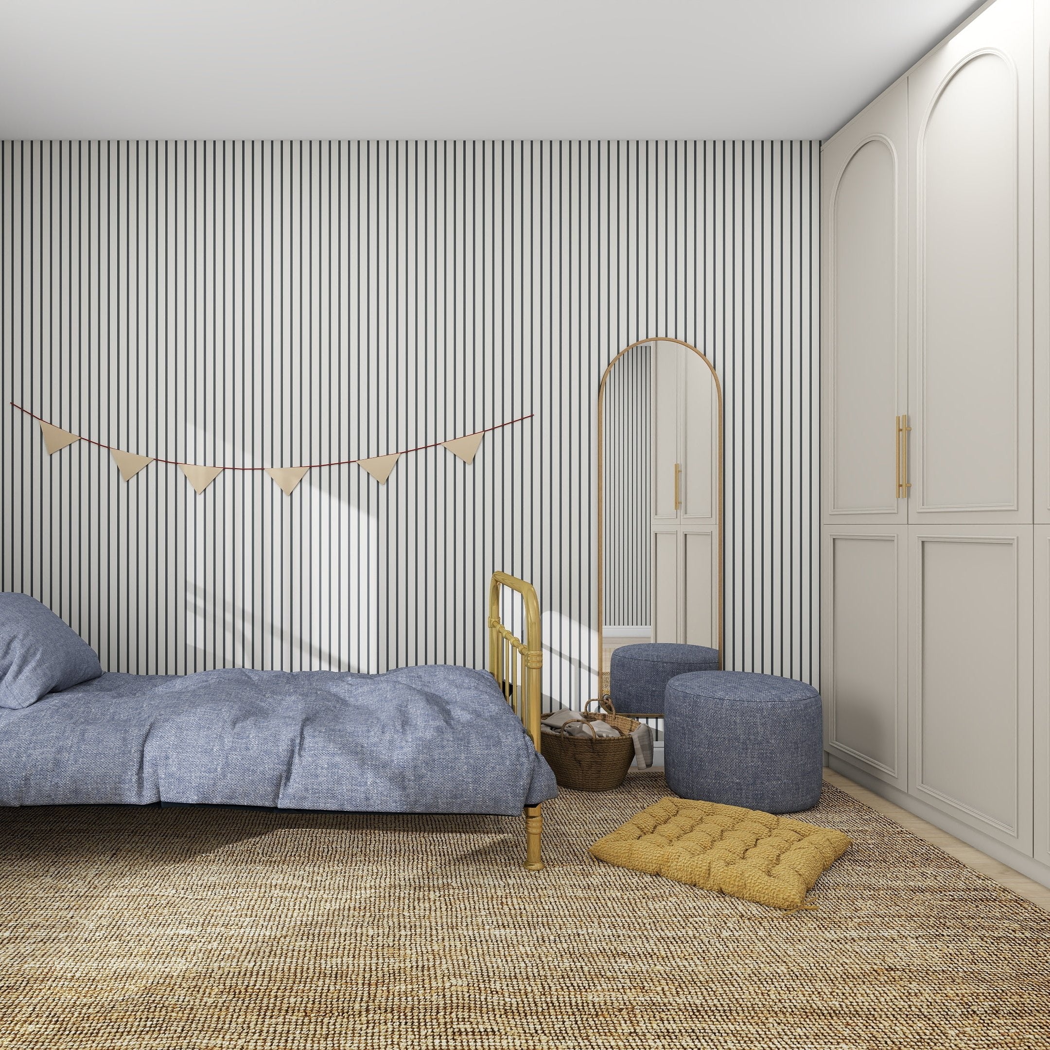 A minimalist bedroom showcases a single bed with blue bedding, a wicker rug, and a yellow floor cushion. The Pinstripe Wallpaper Denim by munks and me complements the golden-framed mirrors quality. Two blue poufs, bunting, and a cream wardrobe complete the look.