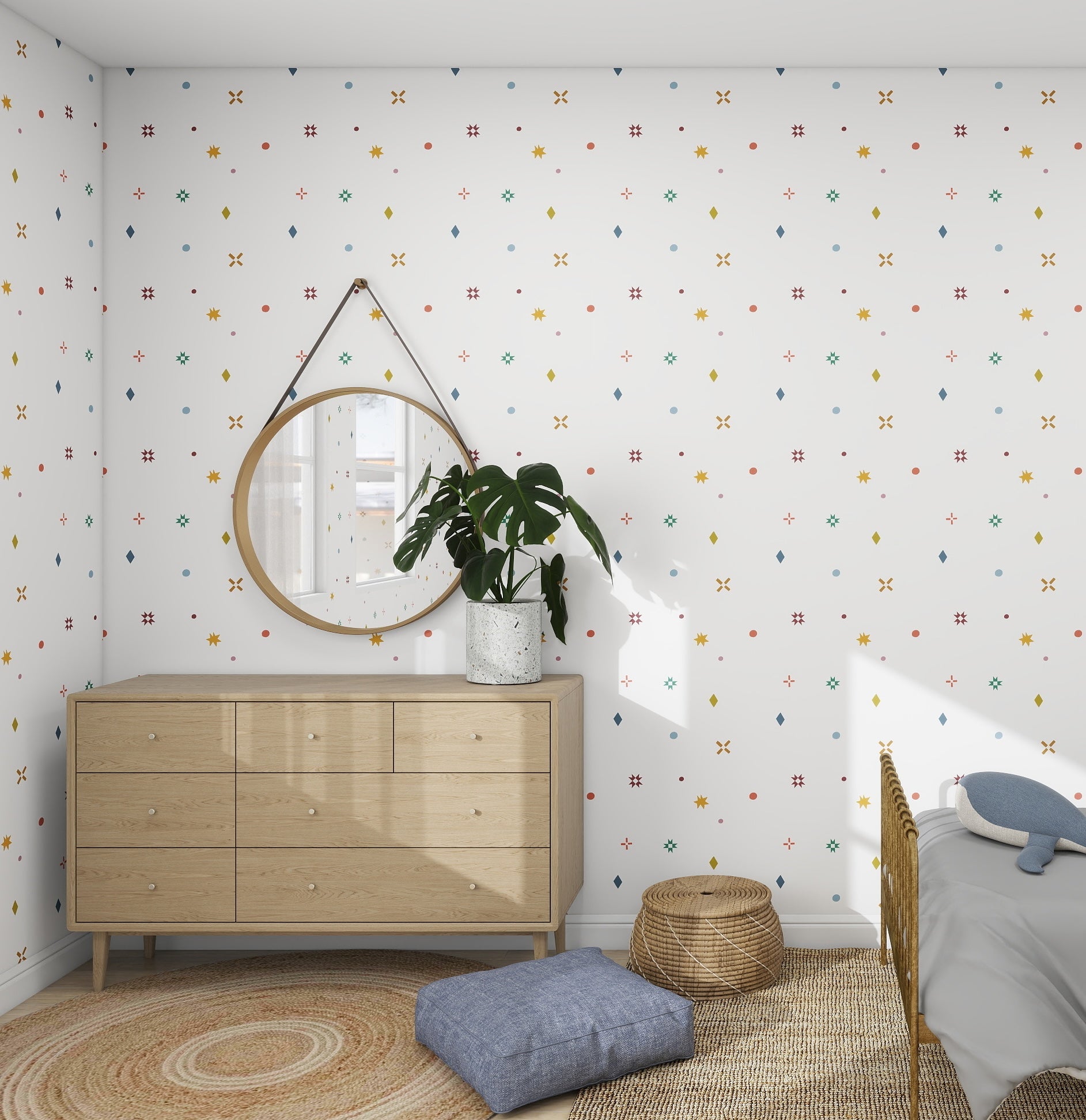 A Scandinavian-inspired bedroom corner features a light wood dresser, round mirror, and potted plant. The space is framed by munks and mes Pebble and Patch Wallpaper Repeat Pattern in Multi on the white walls. A blue pillow and woven basket rest on the floor, bathed in natural light.