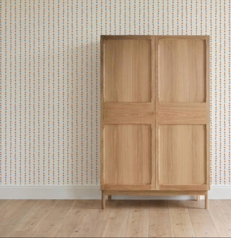 A light wooden cabinet with four panels stands on a wooden floor against a wall adorned with All I See Is Magic Stripe Wallpaper, featuring vertical lines of small colored dots.