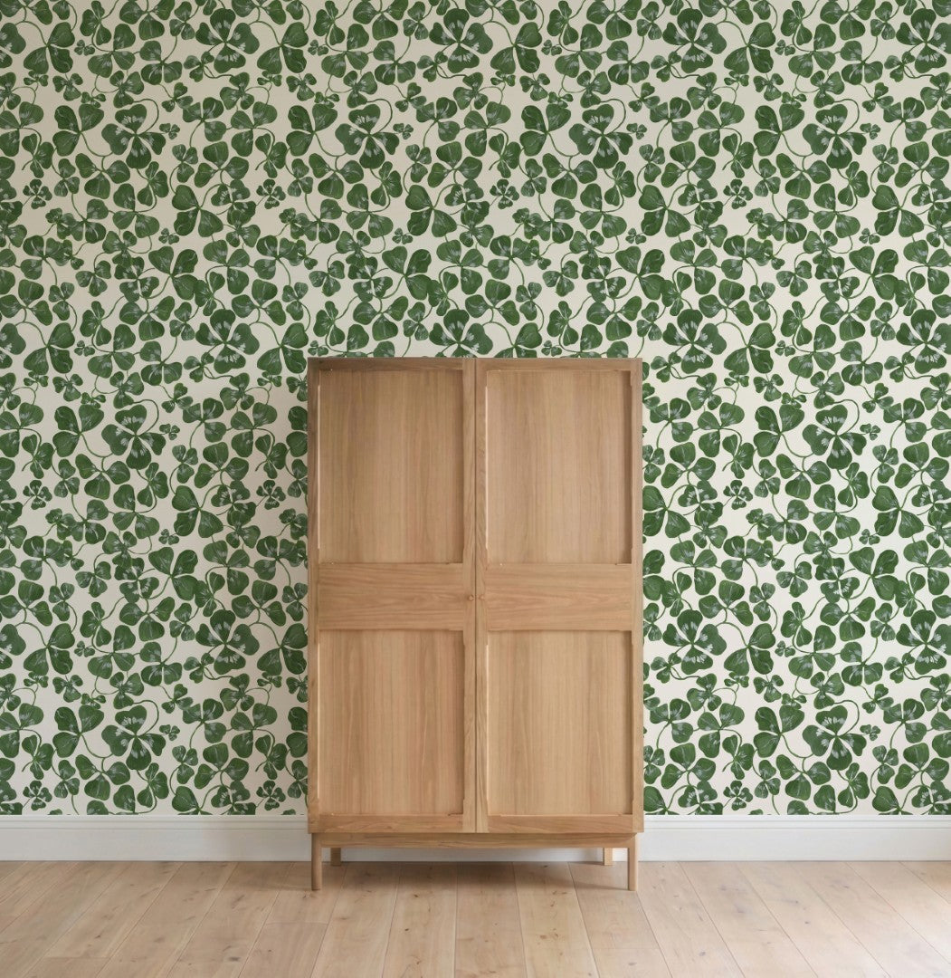 A wooden cabinet with a modern four-panel design stands on a light wood floor against a wall covered in How Lucky We Are Clovers Wallpaper.