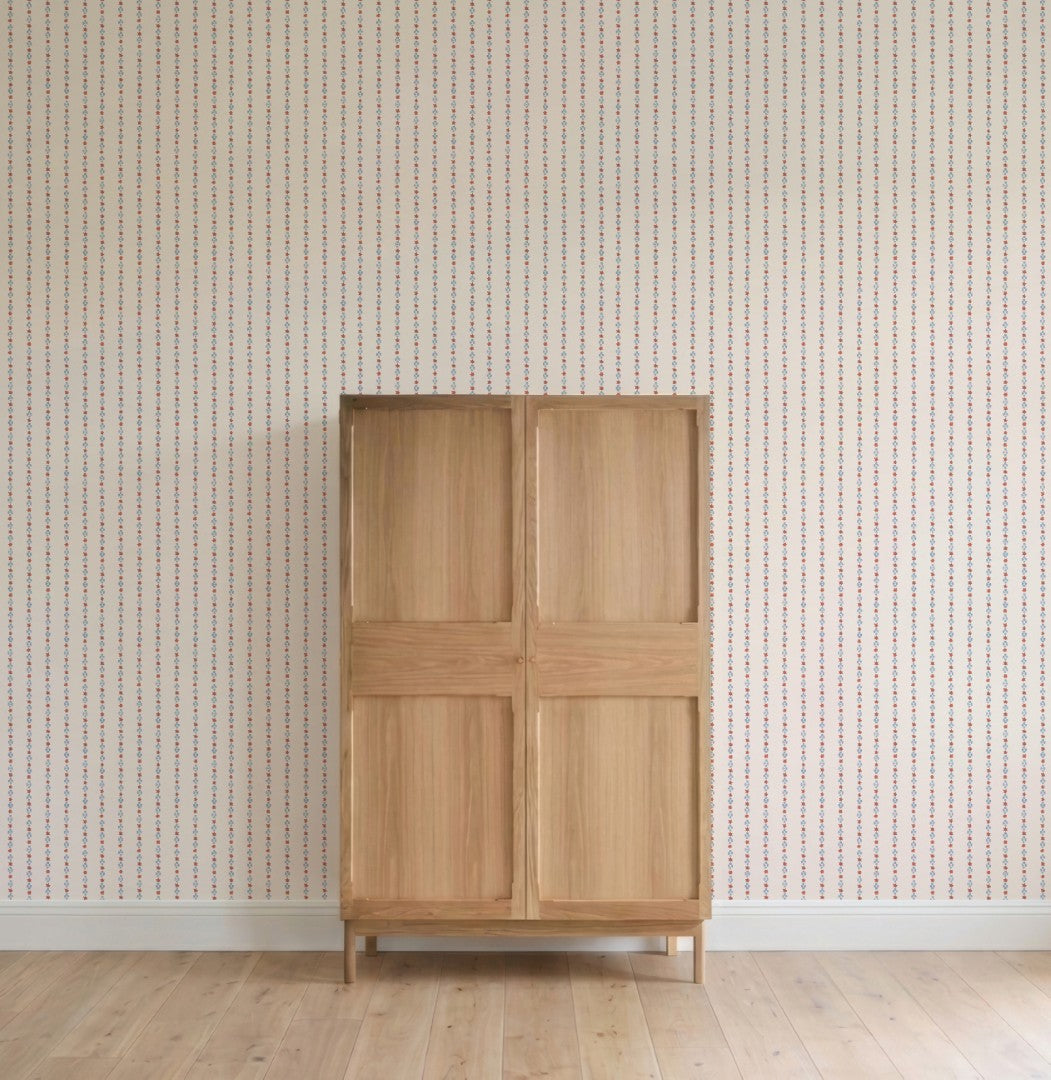 A simple wooden cabinet with four panels stands against a wall adorned with Jacquard Stars Wallpaper, Red, in a room featuring light wood flooring.