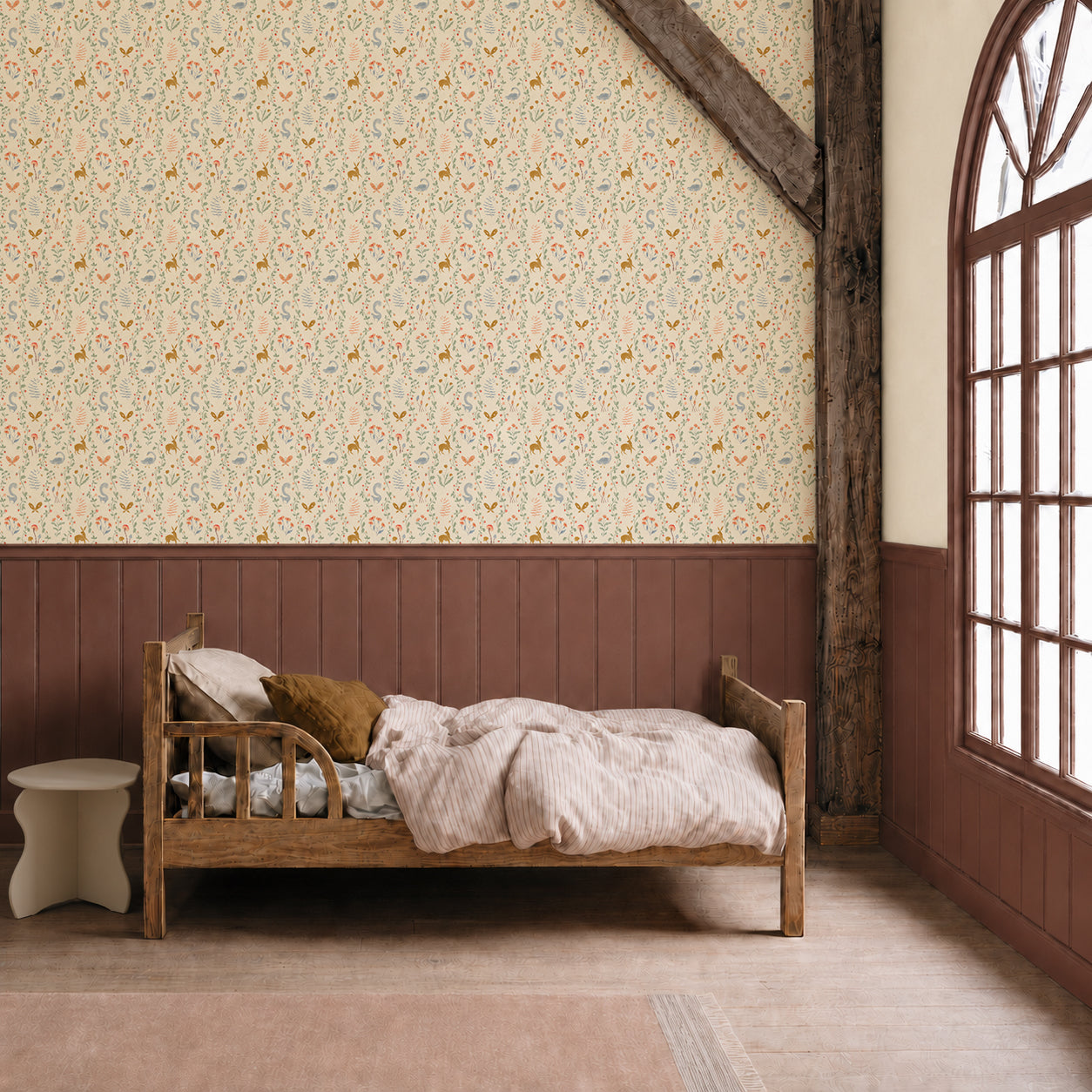 A rustic bedroom with a wooden bed, neutral bedding, a white side table, whimsical Coles Berry Patch Wallpaper featuring delicate florals, wood paneling, and a large arched window letting in natural light.