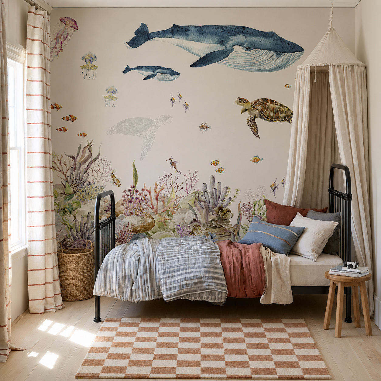Children’s bedroom with a bed, canopy, striped curtains, a checkered rug, and a wall mural featuring whales, a turtle, jellyfish, and vibrant coral and fish—all set against the enchanting Under The Sea Mural, Watercolour wallpaper scene.