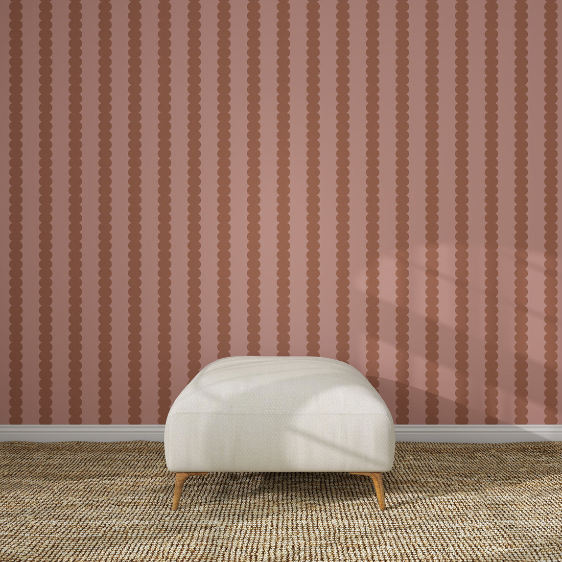 A cream-colored ottoman sits on a textured beige rug in front of Scallop Stripe Wallpaper Toffee Rose. Sunlight casts gentle shadows across the ottoman and floor, highlighting the elegant design.