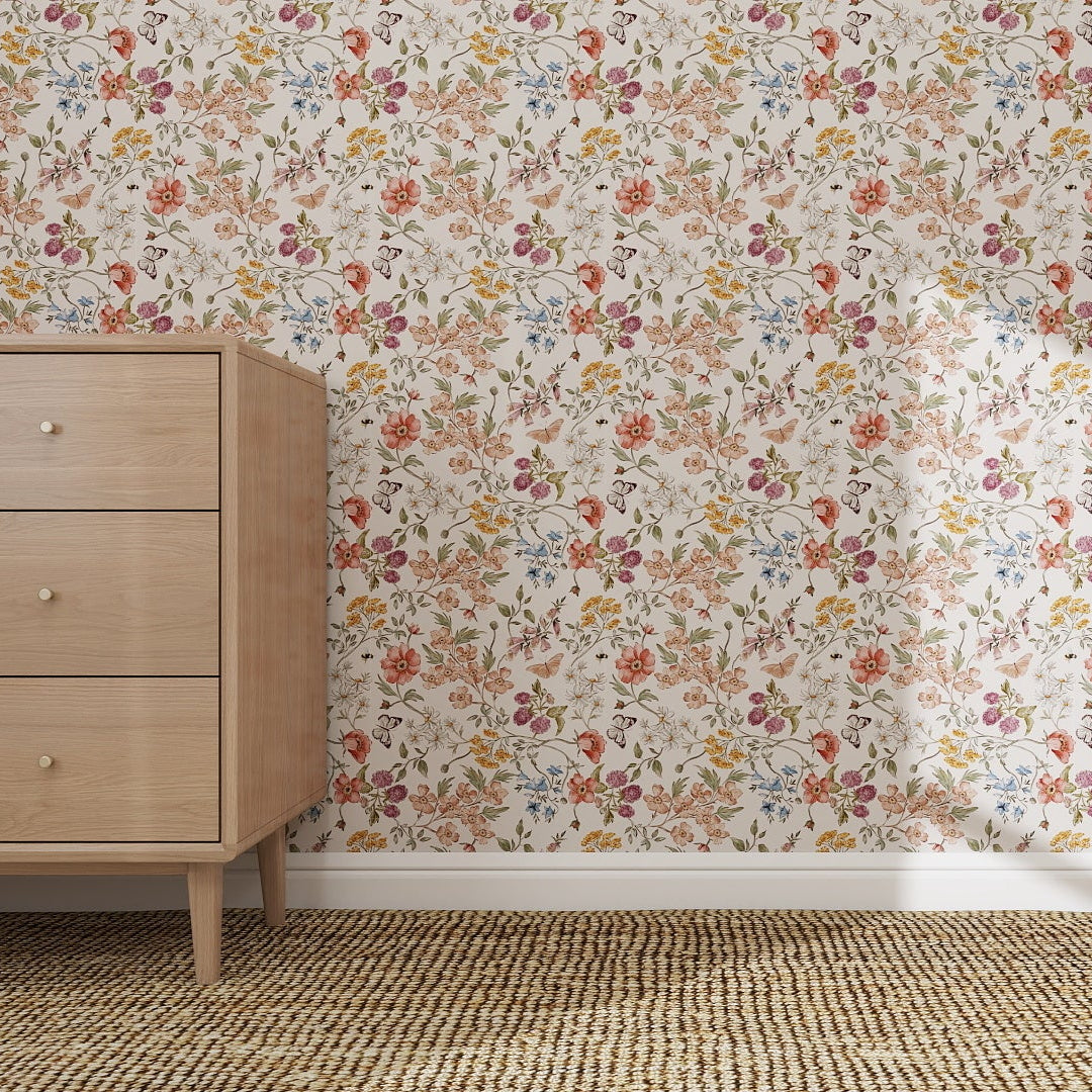 A light wood dresser with three drawers stands on a woven rug beside a wall adorned in Sunlit Butterfly Meadow Wallpaper Repeat Pattern, featuring vibrant red, orange, yellow, and purple flowers with lush green leaves.