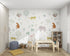 The Wild Wonders Wallpaper Mural by munks and me showcases exotic animals like elephants, tigers, leopards, and sloths in a childrens room. A light wooden table sits on a beige rug, perfectly paired with shelves brimming with toys and books.