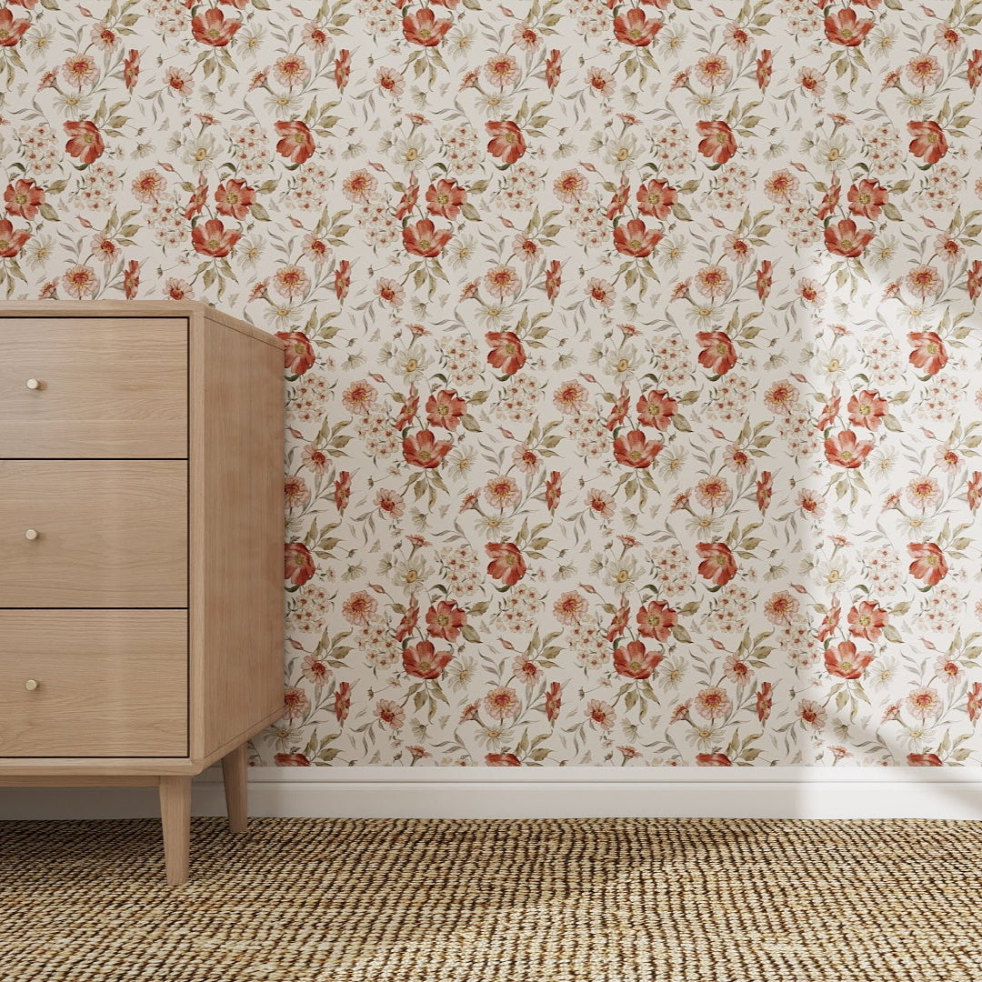 A light wooden three-drawer dresser stands on a woven rug by a wall adorned with Wild Rose Dreams Wallpaper Repeat Pattern, featuring vivid red and orange flowers with green leaves. The scene feels simple, cozy, and vintage.
