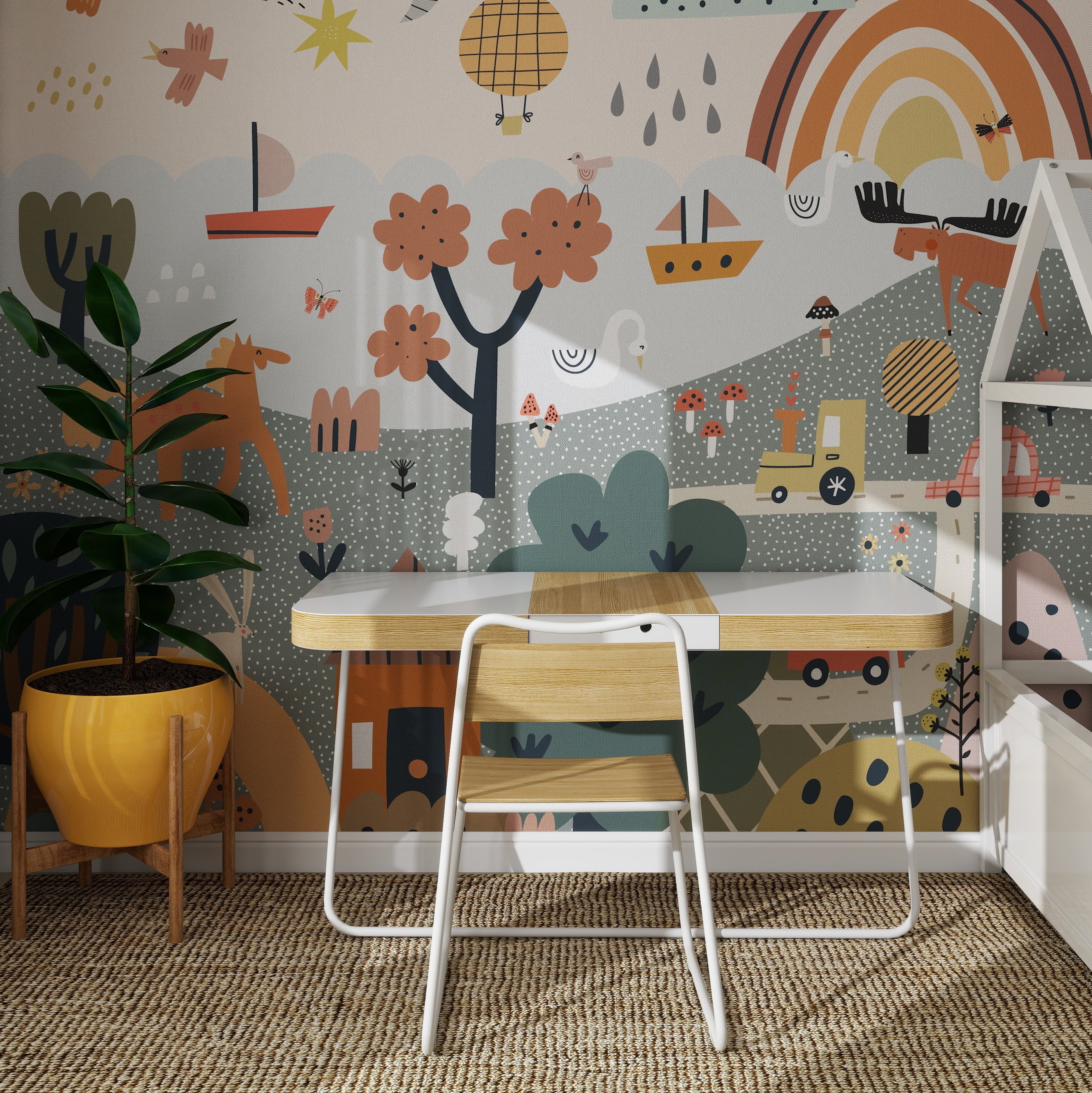 A small wooden desk with a white chair stands on a woven rug before the Wonderpark Wallpaper Mural—a colorful, whimsical rainbow scene with trees, boats, and playful shapes. A potted plant is placed to the left of the desk.