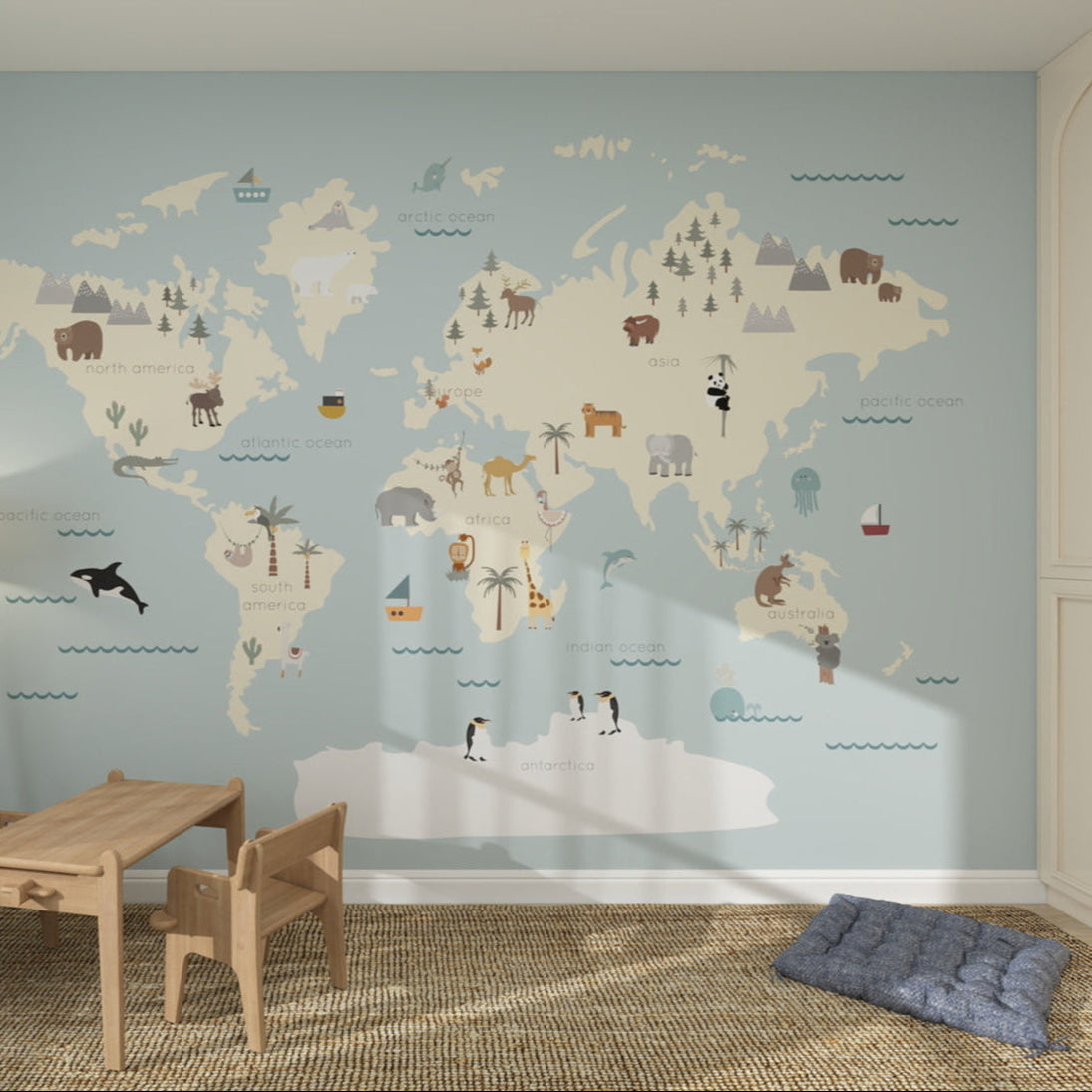 A children’s room with the Character World Map Mural, Blue, featuring illustrated animals and landmarks for each continent. Includes a small wooden table with chairs and a cushion on a woven rug—perfect for little adventurers.