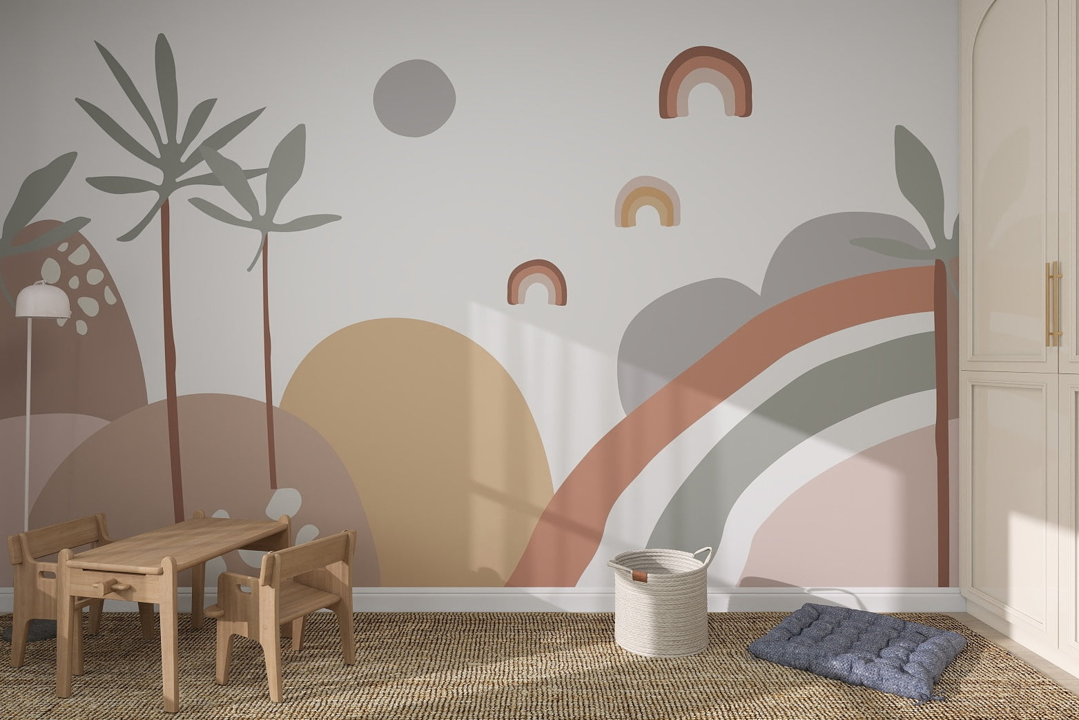 A childrens room with a wooden table and chairs, a basket, and a floor cushion features the Abstract Wren Wallpaper Mural, showcasing rainbows, plants, and shapes in earthy tones on the wall.