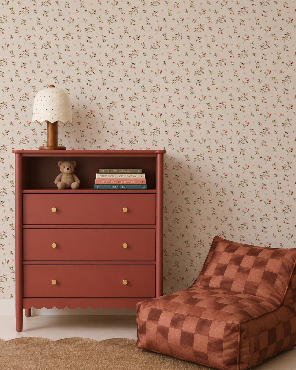 A rust-colored dresser with books, a teddy bear, and a polka-dot lamp sits beside a brown checked lounge chair against Berry and Bramble Wallpaper in a cozy room.
