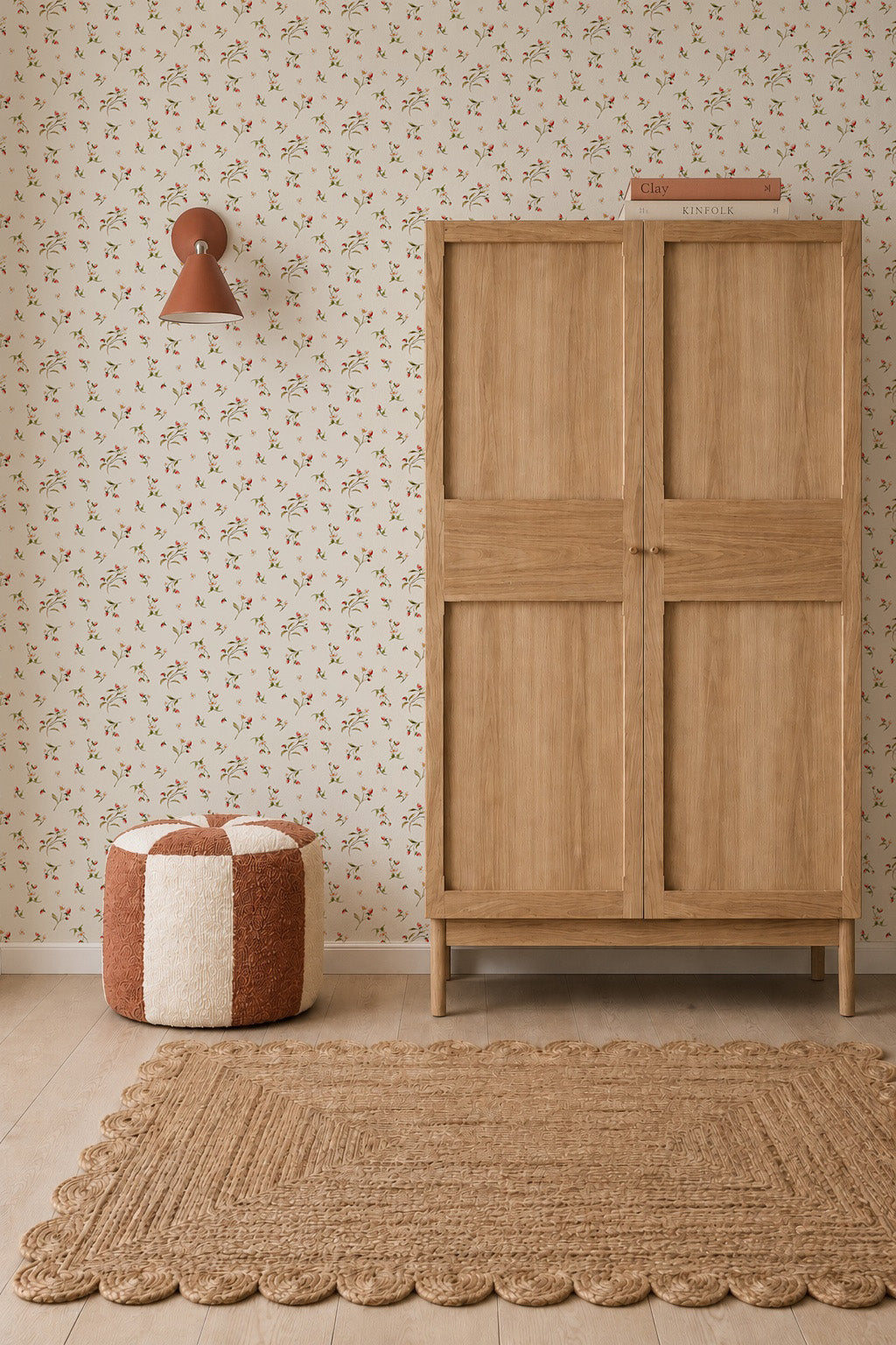 A cozy room featuring a light wood wardrobe with a book on top, a two-toned round pouf, textured natural fiber rug, wall sconce, and Berry and Bramble Wallpaper in soft botanical tones.