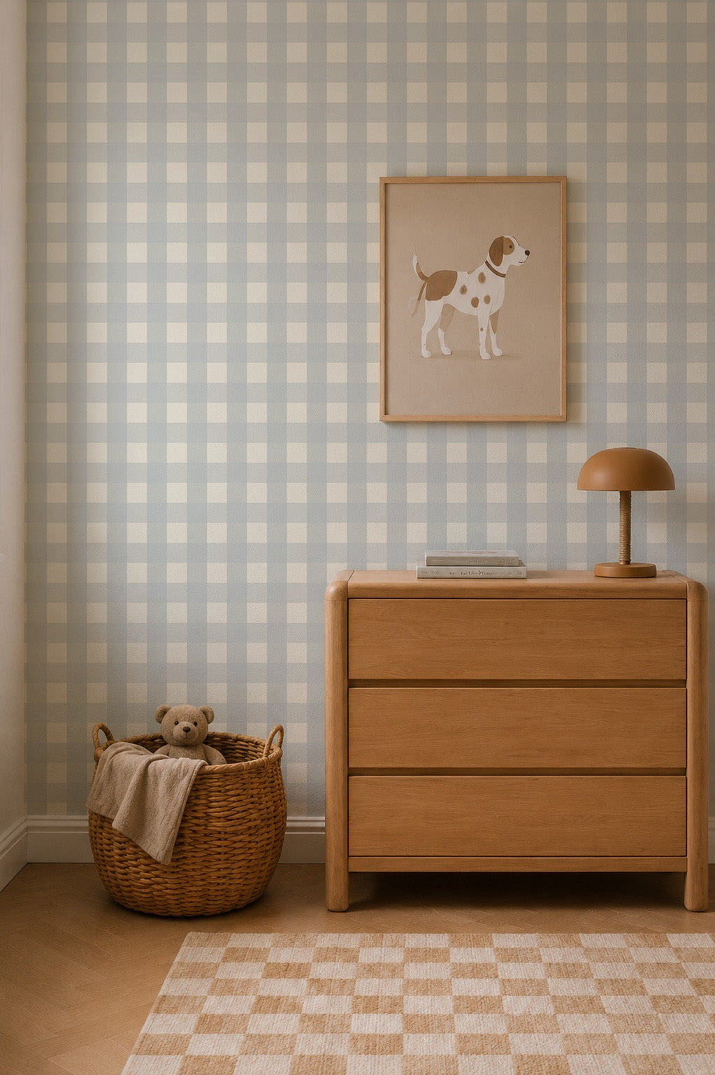 A light wood dresser sits against Large Check Wallpaper, Blue, with a framed dog print above and a wicker basket containing a teddy bear on the floor.