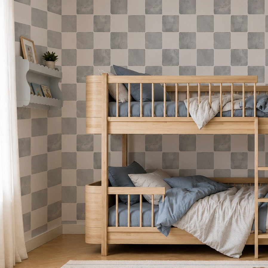 Children’s bedroom with wooden bunk beds, blue and white bedding, Billys Checkered Wallpaper in Blue, a shelf with toys and books, a striped rug, a wooden toy car on the floor, and an open book lying on the rug.