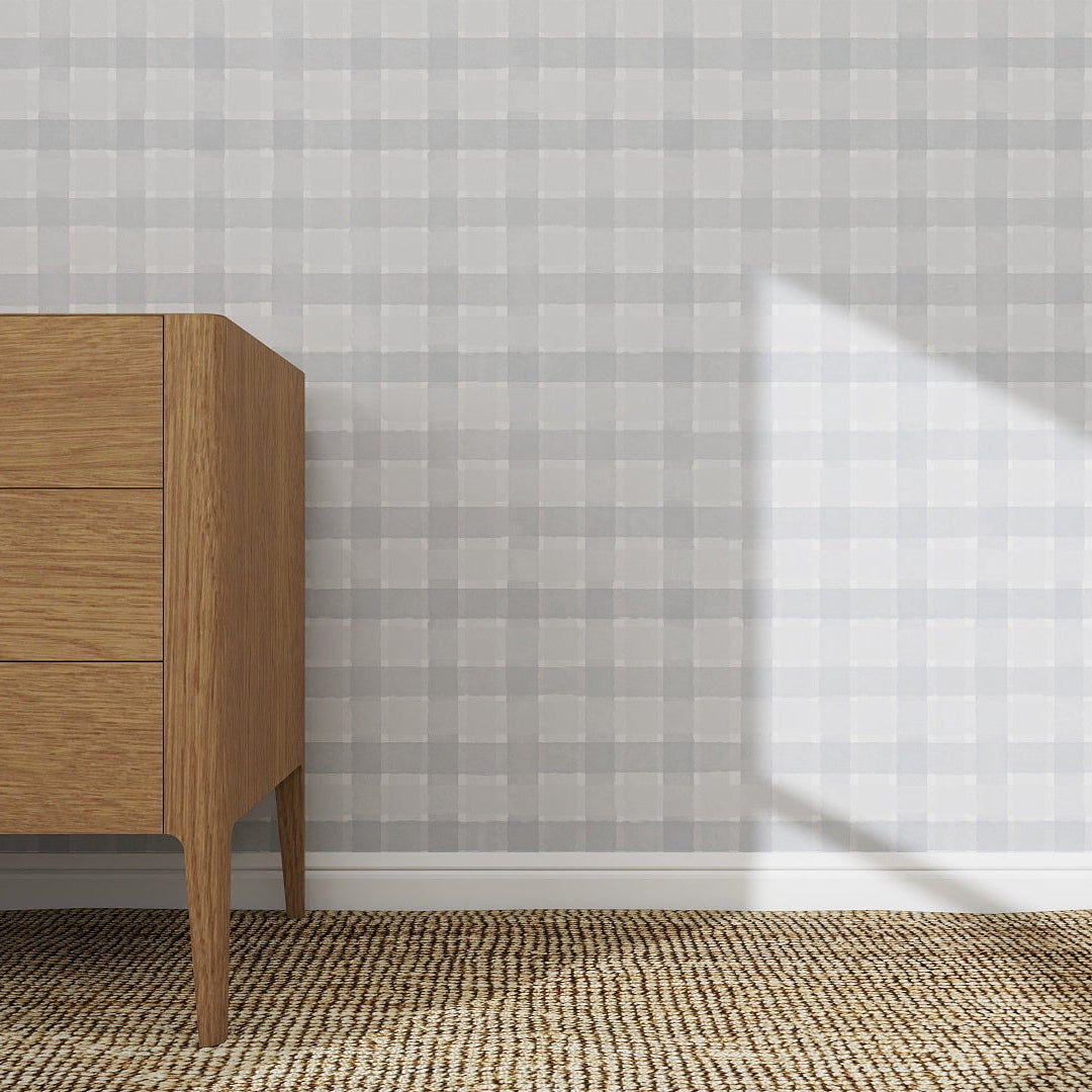 A wooden dresser stands on a woven carpet by a light gray wall decorated with the Checkered Wallpaper Repeat Pattern Blue | Sample, as sunlight casts a triangular shadow, highlighting the wallpapers quality.