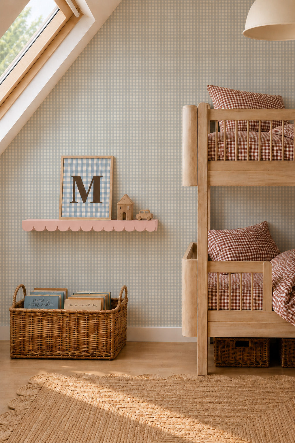 A cozy children’s room with wooden bunk beds, checked bedding, a wicker basket of books, a pink shelf with decor items, and a window letting in natural light. A sample of the Mini Check Wallpaper in Blue brings a playful touch to the walls while showcasing available colour options and quality for the perfect finishing detail.