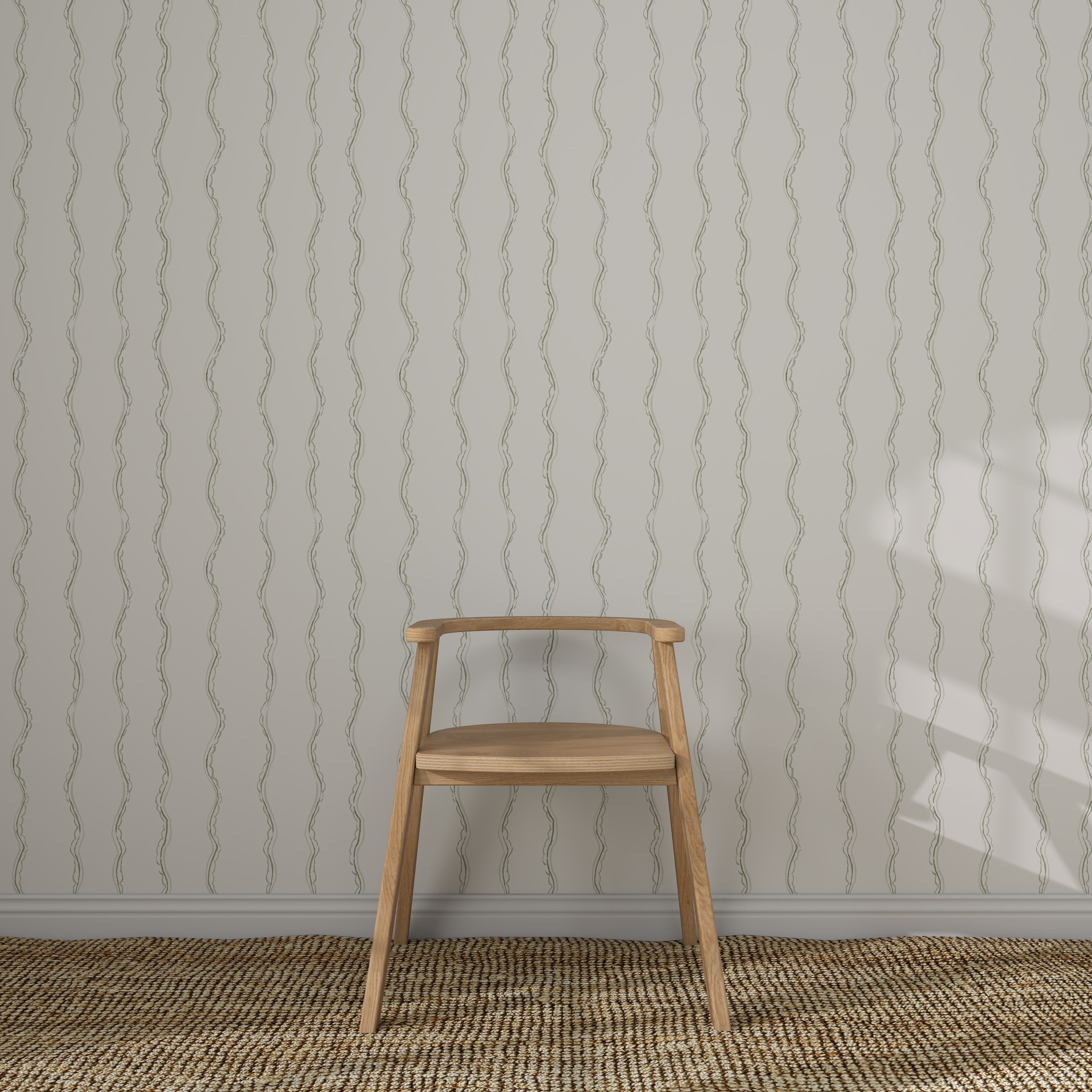 A light wooden chair with a curved backrest sits on a woven rug before a white wall featuring Ribbon Stripe Wallpaper in Sage. Sunlight casts partial shadows, creating an elegant children&