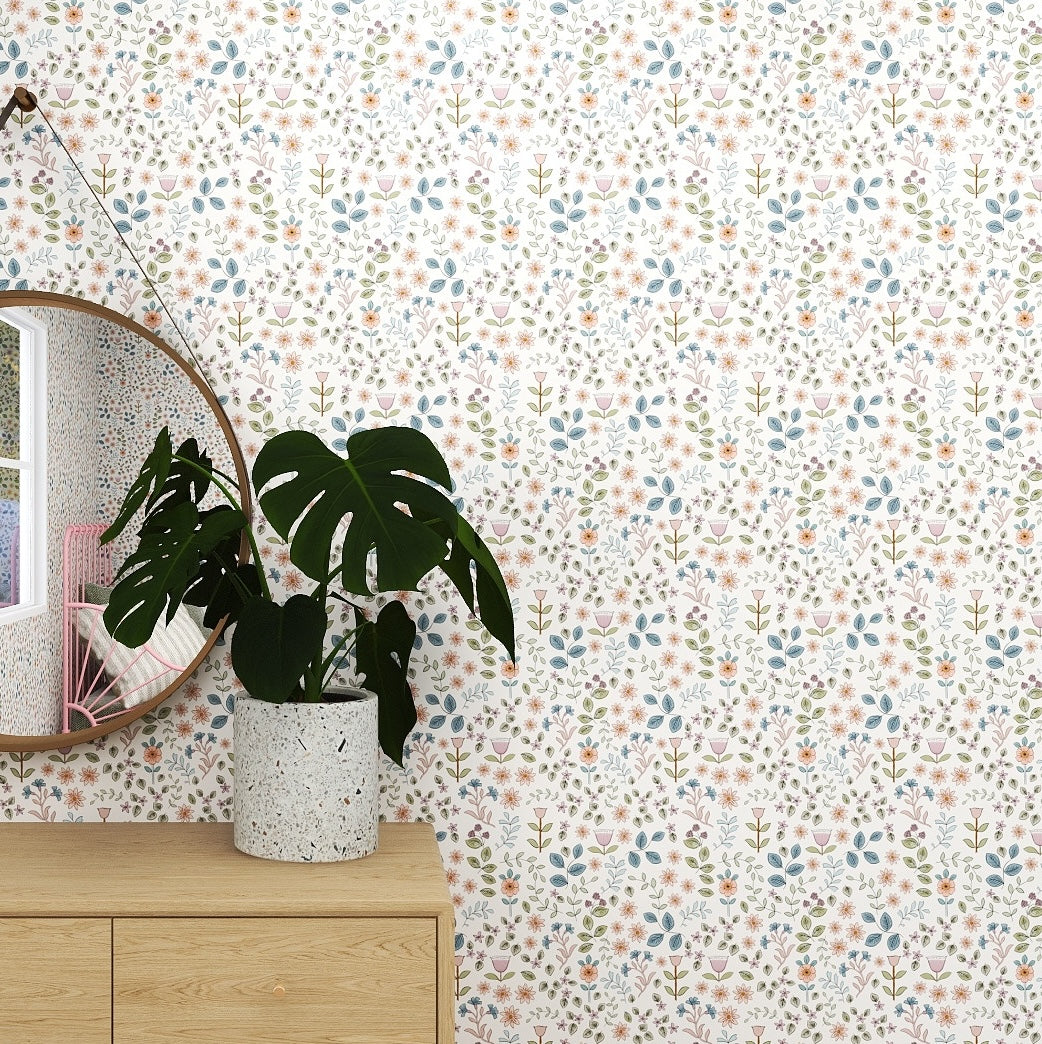 A round mirror hangs on a Ditsy Blooms Wallpaper Repeat Pattern wall above a light wood cabinet. A potted plant with large green leaves sits on the cabinet, its reflection enhancing the whimsical decor.