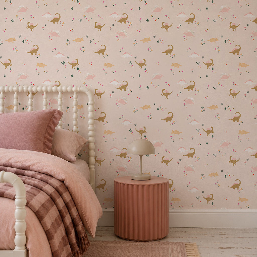 A cozy bedroom with a bed in pink linens, a round pink nightstand with a beige lamp, and playful Dixie Dinosaur Wallpaper featuring deer and florals on a light pink background.