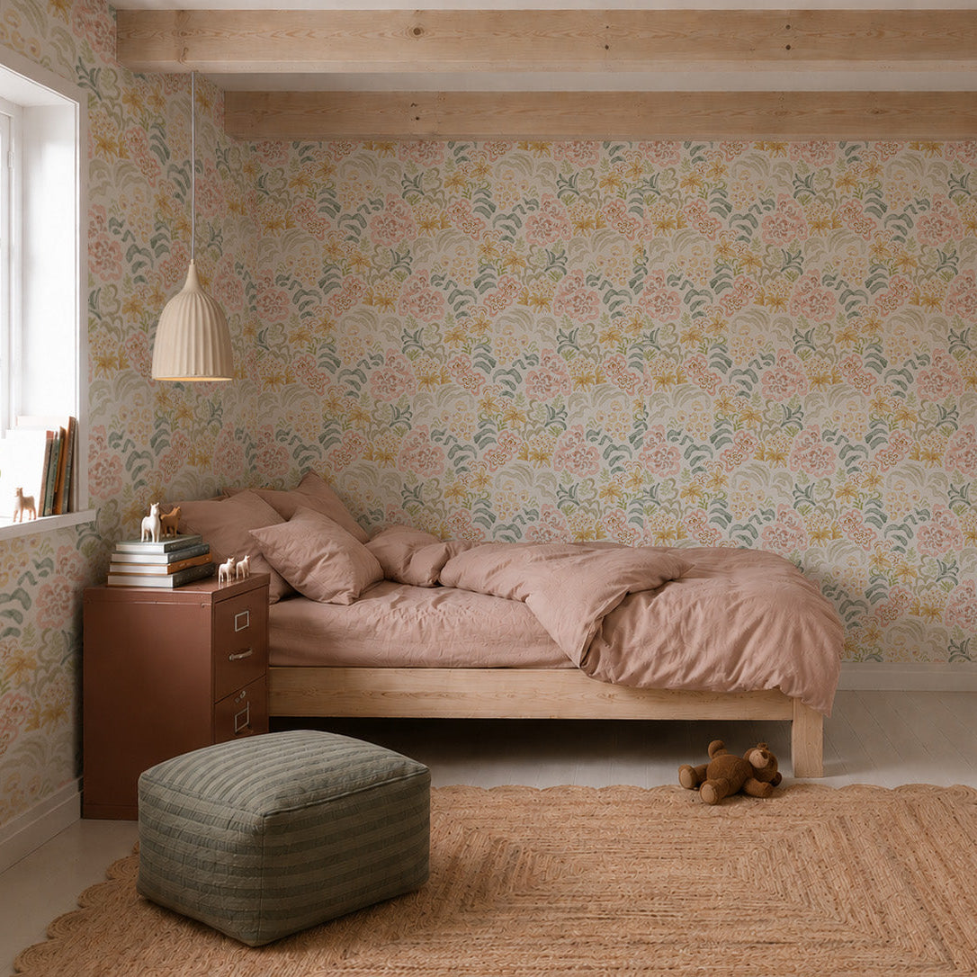 A cozy bedroom features a wooden bed with dusty pink bedding, Floret Dreamscape Wallpaper adding a whimsical touch to the walls, a brown nightstand stacked with books, a woven rug, a green ottoman, a pendant lamp overhead, and a teddy bear resting on the floor as natural light streams in from the window.