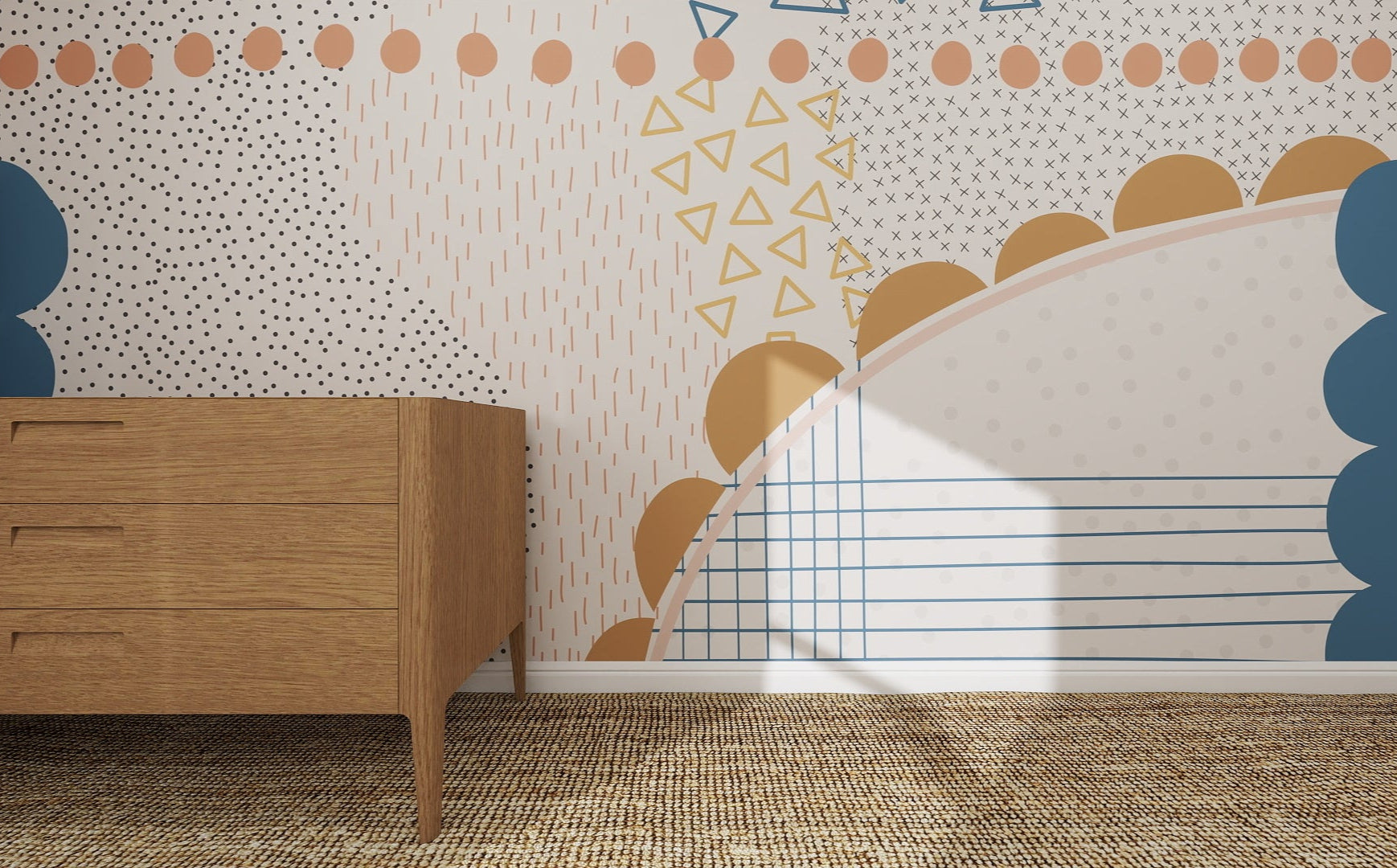 A wooden dresser stands on a woven rug before a wall adorned with the Evie Abstract Wallpaper Mural, featuring blue, mustard, and beige dots, triangles, scallops, and lines. Sunlight highlights this colorful setting.
