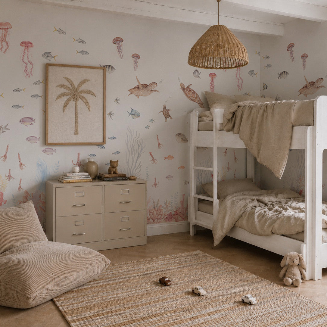 Cozy kids’ bedroom with a Fish Tank Mural, white bunk bed with beige bedding, wicker pendant lamp, dresser, palm tree artwork, plush toys, and natural woven rug on a wooden floor. Sunlight streams in through the window.