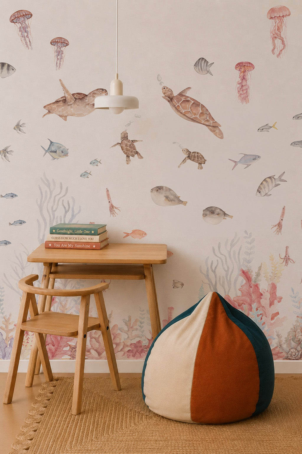 Children’s room featuring a wooden desk and chair, books, pendant light, two-tone bean bag, and the Fish Tank Mural—a watercolor-style ocean wall art with sea creatures and corals that creates a charming underwater effect.