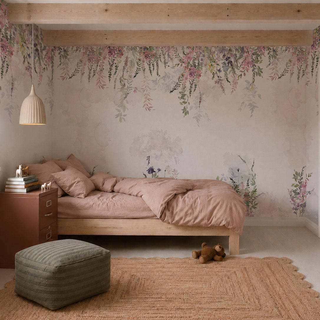 A cozy bedroom features the Florence Florals Mural as wallpaper, a wooden bed with pink bedding, elegant nursery decor, a brown nightstand with books and plants, a woven rug, green pouf, teddy bear, and a pendant light from the beamed ceiling.