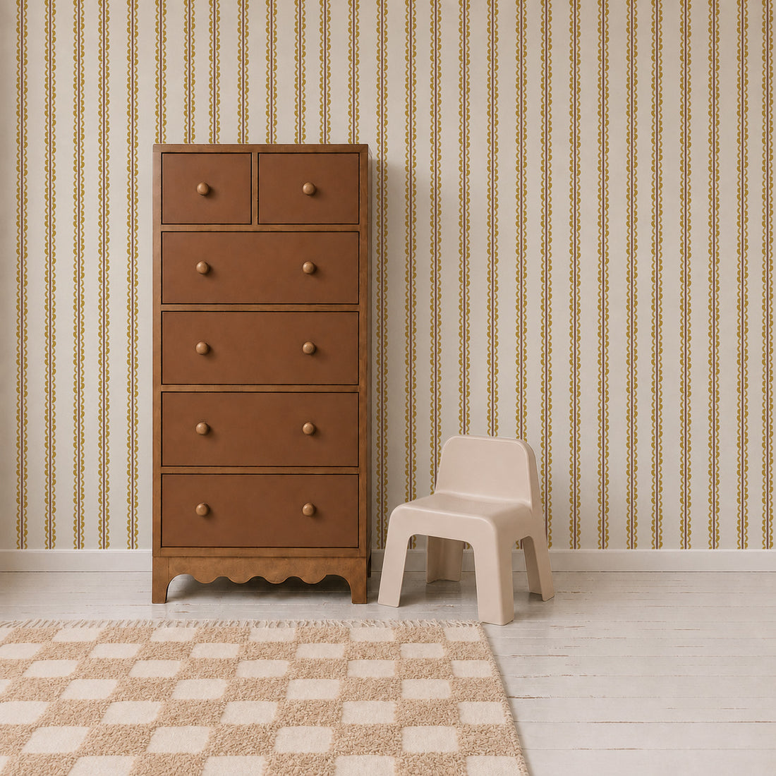 A brown wooden dresser with six drawers stands next to a small beige plastic chair on a white floor, with a checkered rug and Folk Scallop Stripe Wallpaper in Ochre & Mocha in the background.