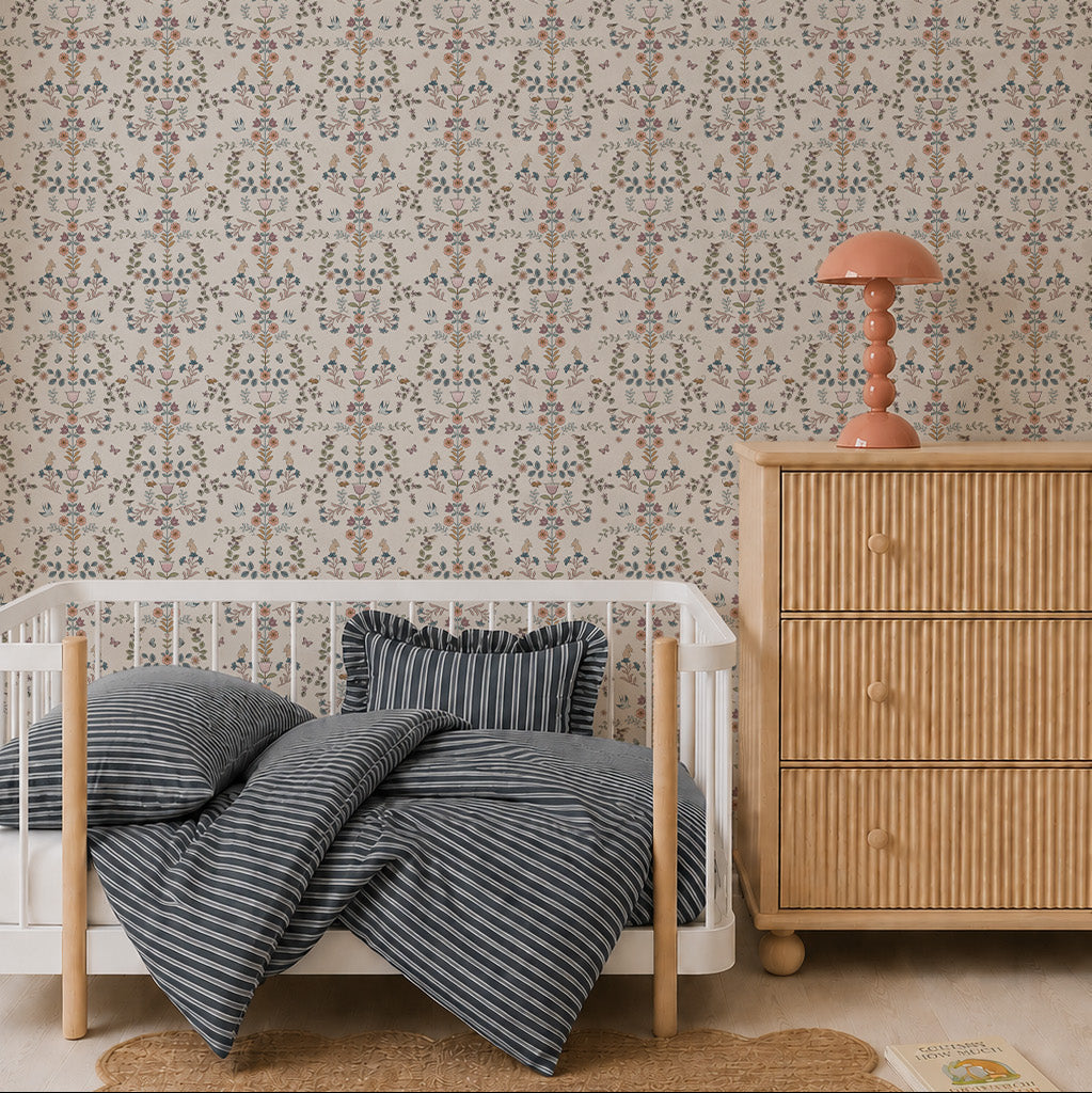 A cozy nursery features a rattan dresser, a white crib with blue-striped bedding, a scalloped jute rug, and Forest Tales Wallpaper. A pink mushroom-shaped lamp sits on the dresser, with a book on the floor nearby.