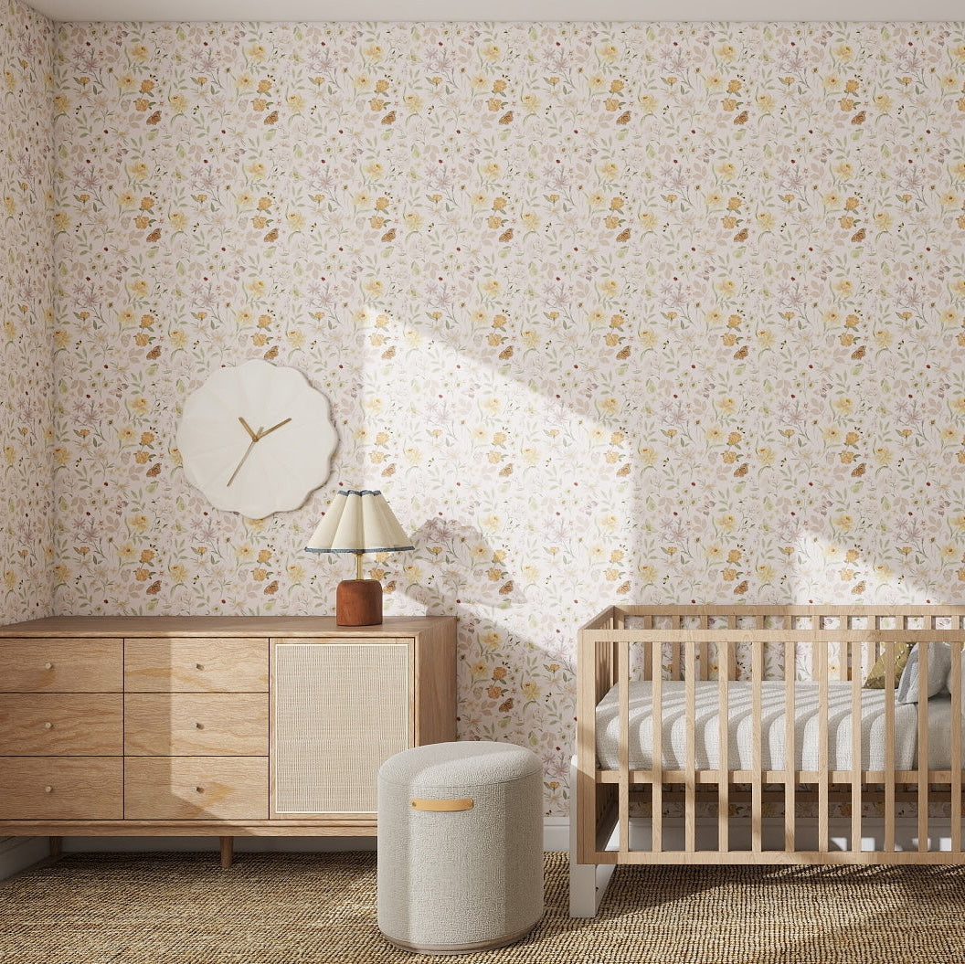 A nursery with Garden Symphony Wallpaper Repeat Pattern, a light wood crib, a matching dresser with lamp, a decorative wall clock, and a round cushioned stool on a woven rug. Sunlight streams in from an unseen window.
