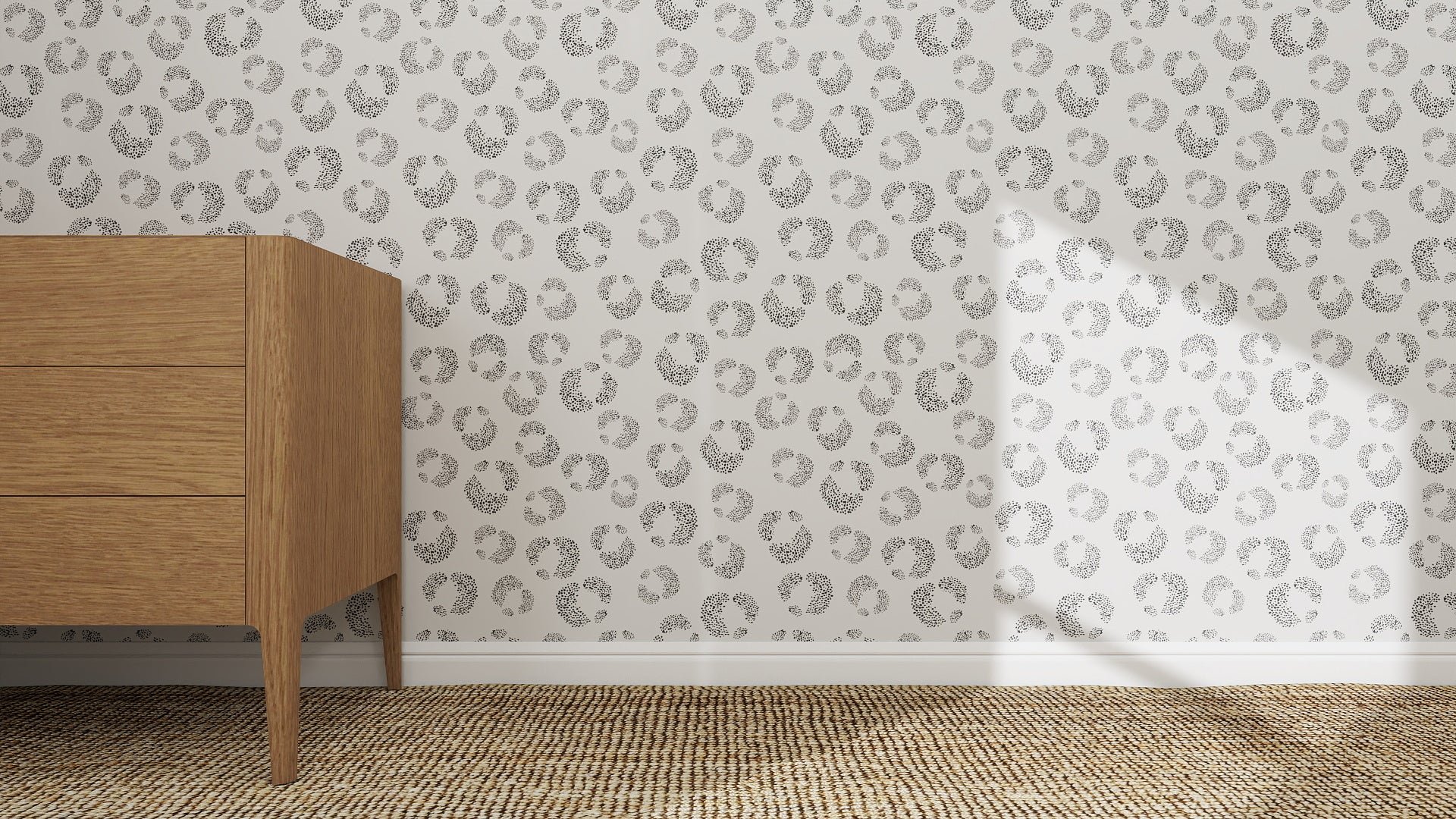 A wooden dresser stands on a textured carpet beside a white wall decorated with whimsical art and Hallie Leopard Print Wallpaper Repeat Pattern in Charcoal. Sunlight casts shadows across the floor, highlighting the room’s playful charm.
