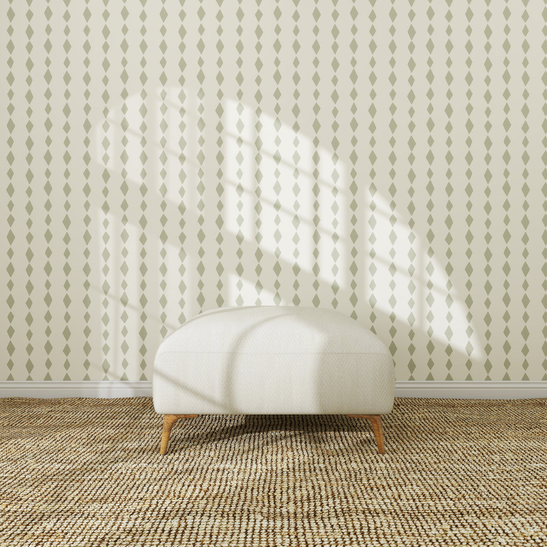 A white upholstered ottoman sits on a textured woven rug in front of the green Jolly Jester Wallpaper Sample, sunlight highlighting its pattern and casting window shadows across the scene.