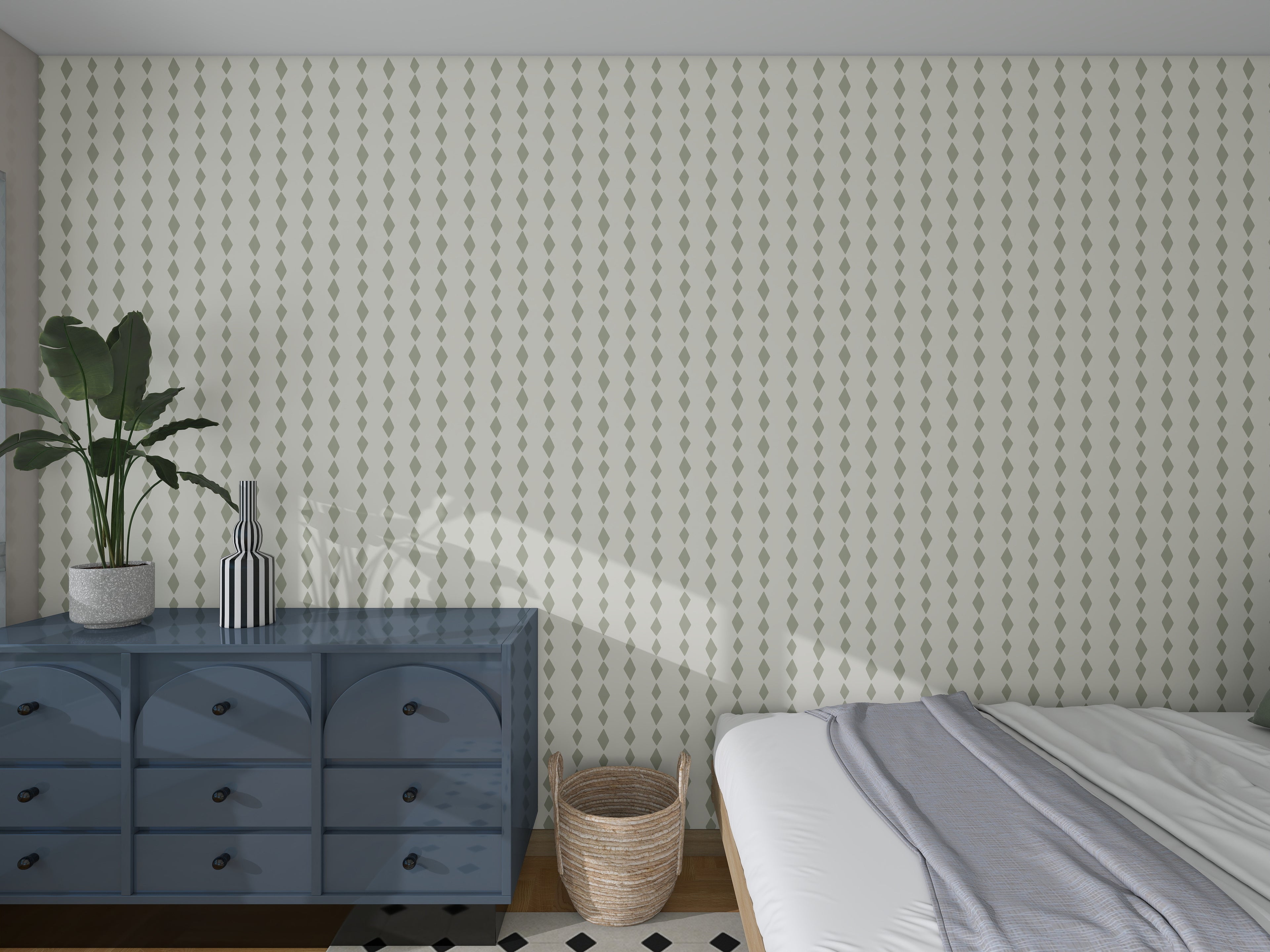 A bedroom with Jolly Jester Wallpaper Repeat Sage Green, a blue dresser with decor, a plant, woven basket, and neatly made white and gray bed. Sunlight streams onto the wall and floor.