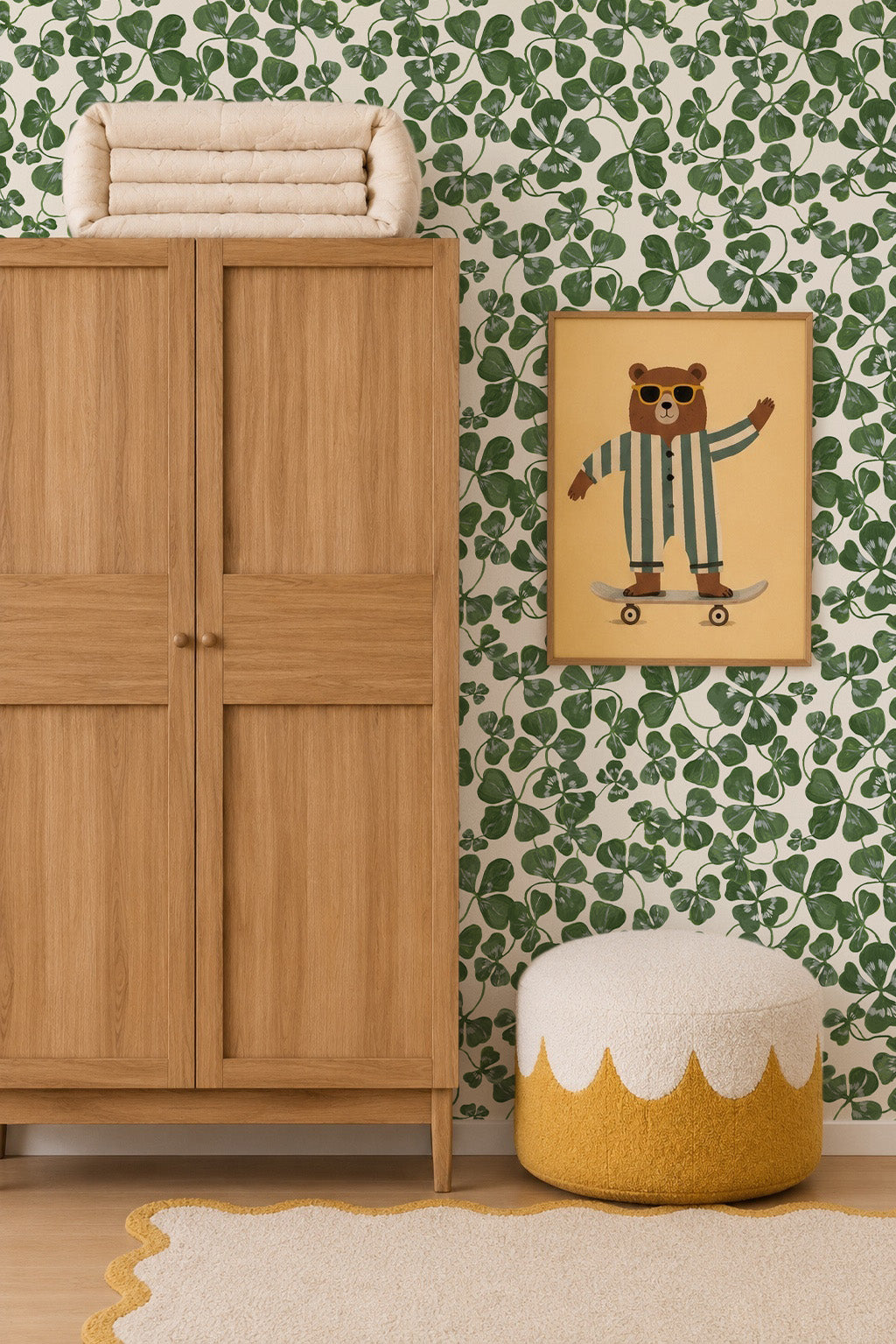 A cozy children’s room featuring a wooden wardrobe, yellow and white pouf, cream rug, framed skateboarding bear art, and playful How Lucky We Are Clovers Wallpaper with green leaf patterns.
