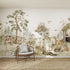 The Into The Forest Wallpaper Mural features illustrated foxes, deer, badgers, squirrels, rabbits, and birds among lush trees and greenery. A wooden chair with a cushion sits in front on a woven rug.