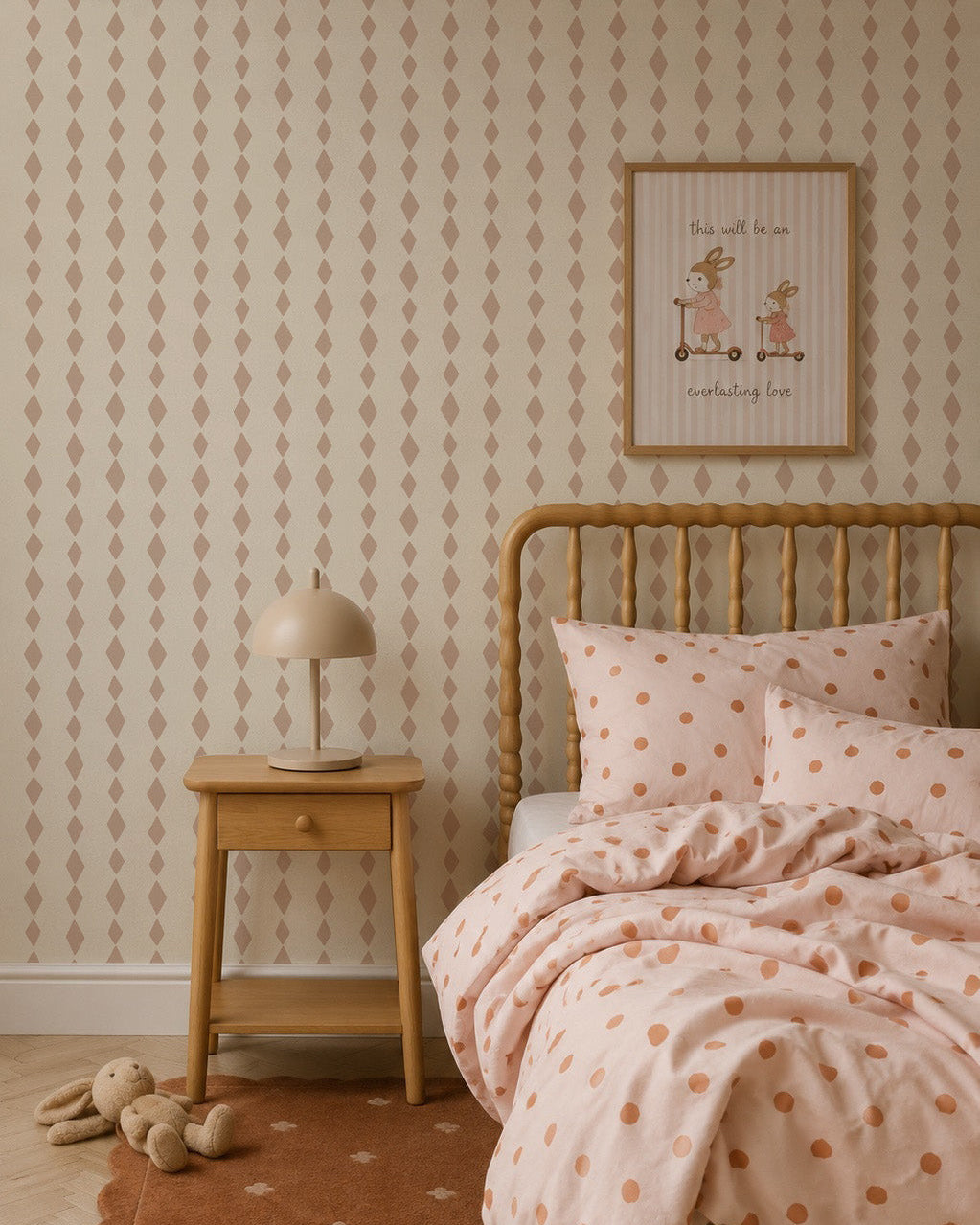Cozy bedroom with a wooden bed, polka dot bedding, matching rug, small wooden nightstand with a beige lamp, and a framed cute animal print on charming Jolly Jester Wallpaper in pink.