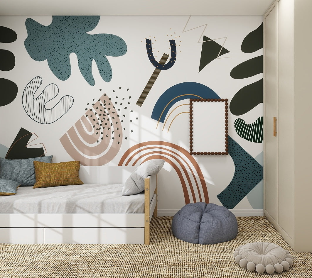 A modern kids bedroom with a wooden bed, colorful pillows, poufs, and a woven rug. The wall is decorated with the Little Erin Abstract Wallpaper Mural | Blue, featuring bold shapes in green, blue, brown, and black hues with a framed mirror centered.
